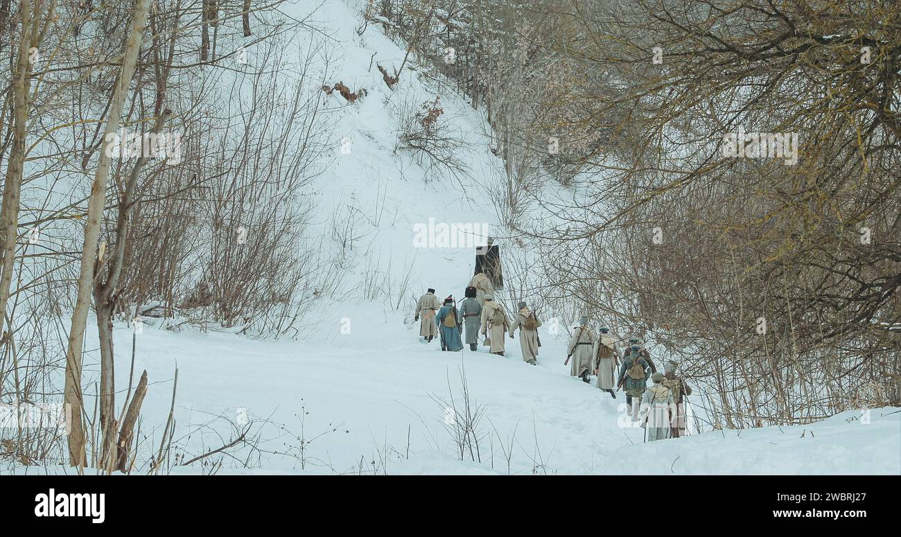 Als Soldaten der Weißen Garde verkleidete Männer der kaiserlichen russischen Armee im russischen Bürgerkrieg, die durch den schneebedeckten Winterwald marschieren. Historische Nachstellung von Stockfoto