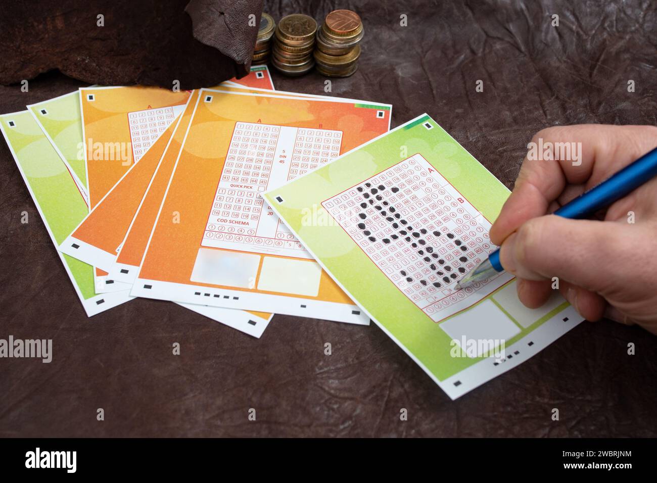 Männliche Hand, die Zahlen auf einem Lottoschein in Form eines Dollarwährungssymbols auf echtem Leder wählt Stockfoto