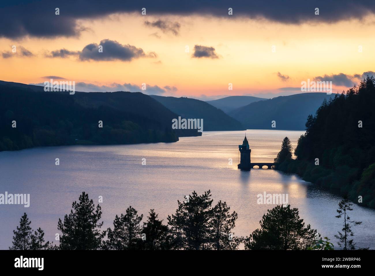 Lake Vyrnwy, in der Mitte von Wales, einer Gegend von außergewöhnlicher natürlicher Schönheit, bei Sonnenuntergang. Der orange Himmel spiegelt sich im ruhigen Wasser des Sees Stockfoto