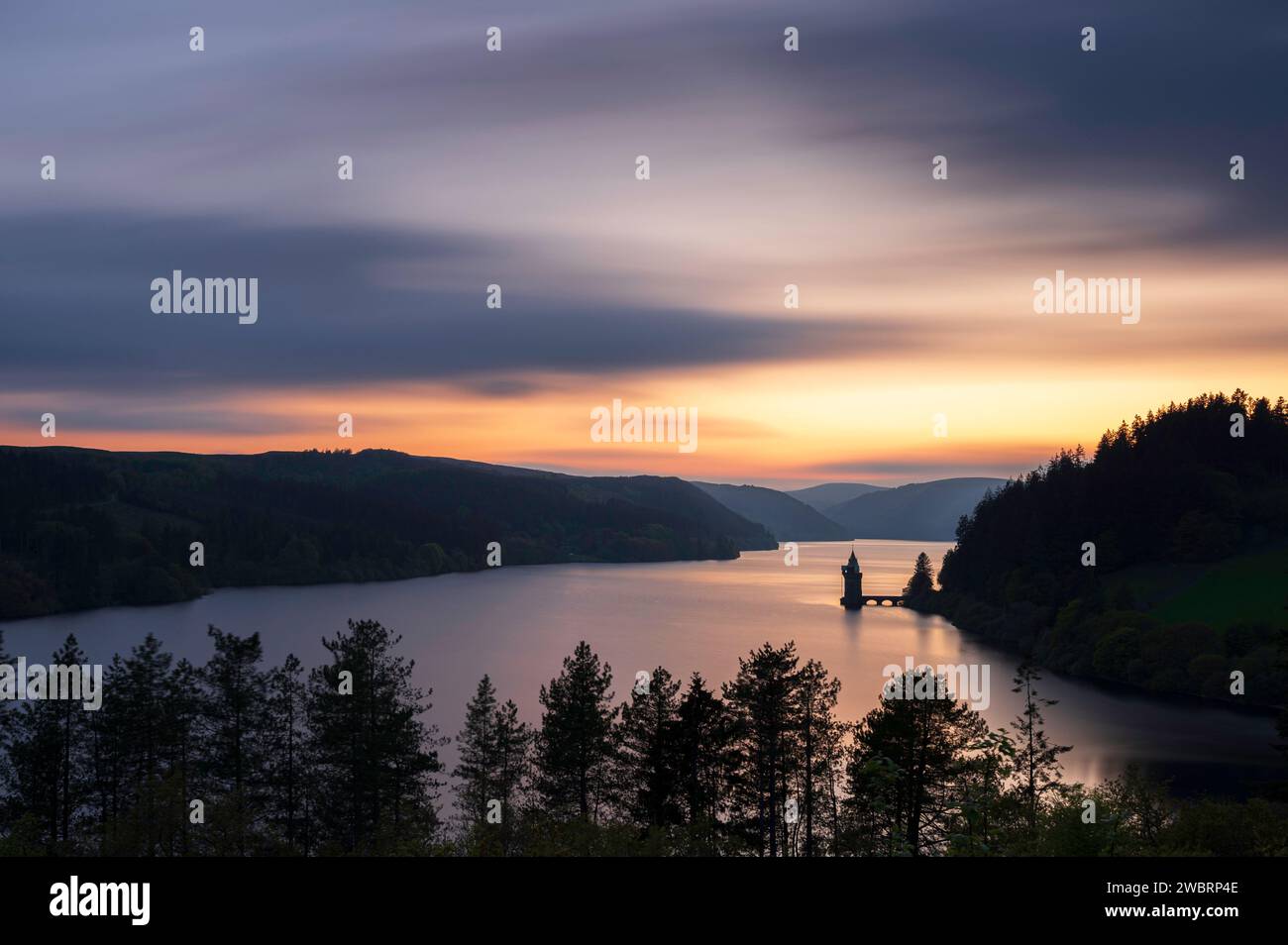 Lake Vyrnwy, in der Mitte von Wales, einer Gegend von außergewöhnlicher natürlicher Schönheit, bei Sonnenuntergang. Der orange Himmel spiegelt sich im ruhigen Wasser des Sees Stockfoto