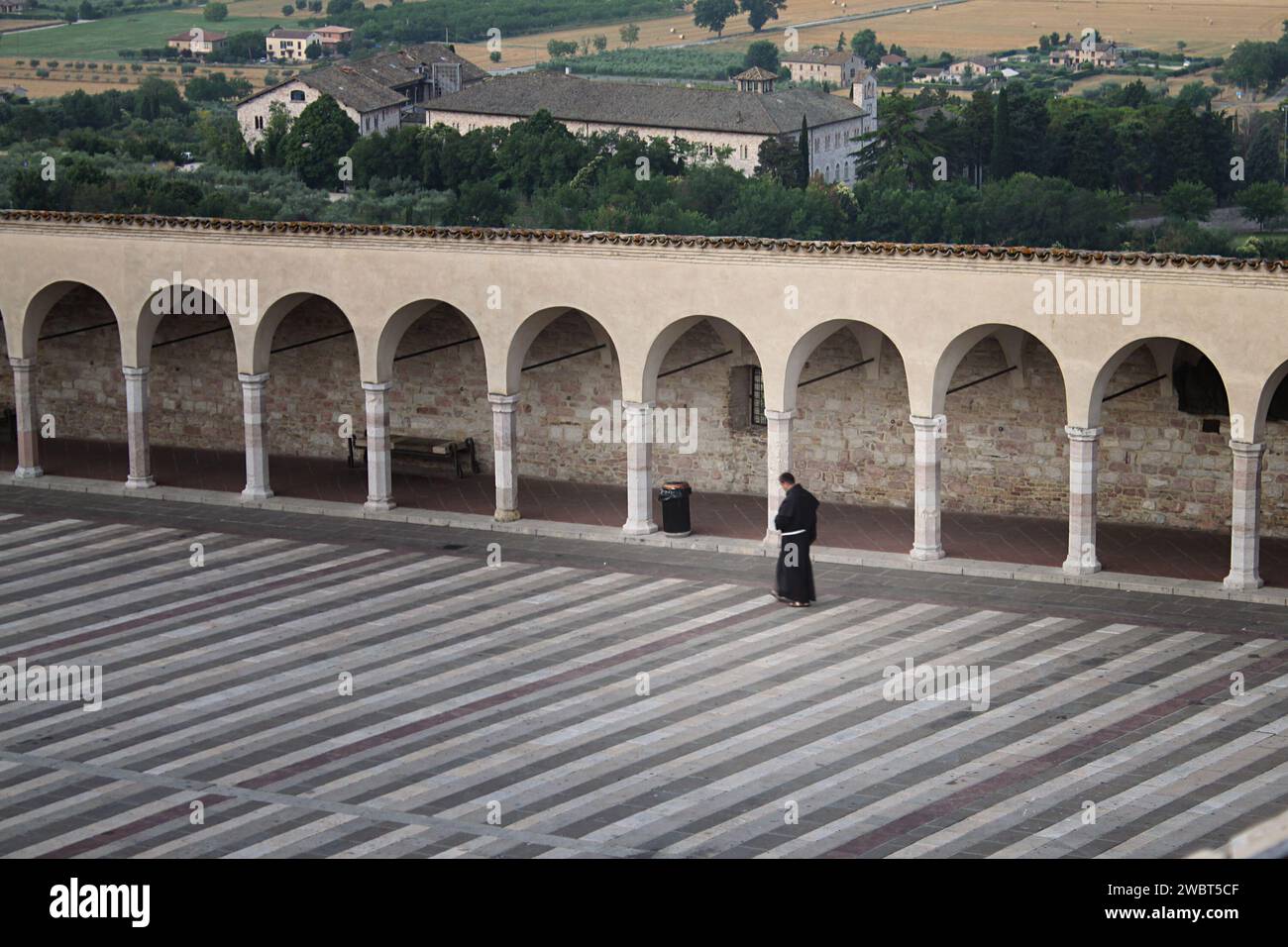 Ein Franziskanerbruder in traditionellen Gewändern, der entlang der Bögen der Kathedrale des Heiligen Franziskus von Assisi in Italien spaziert. Stockfoto