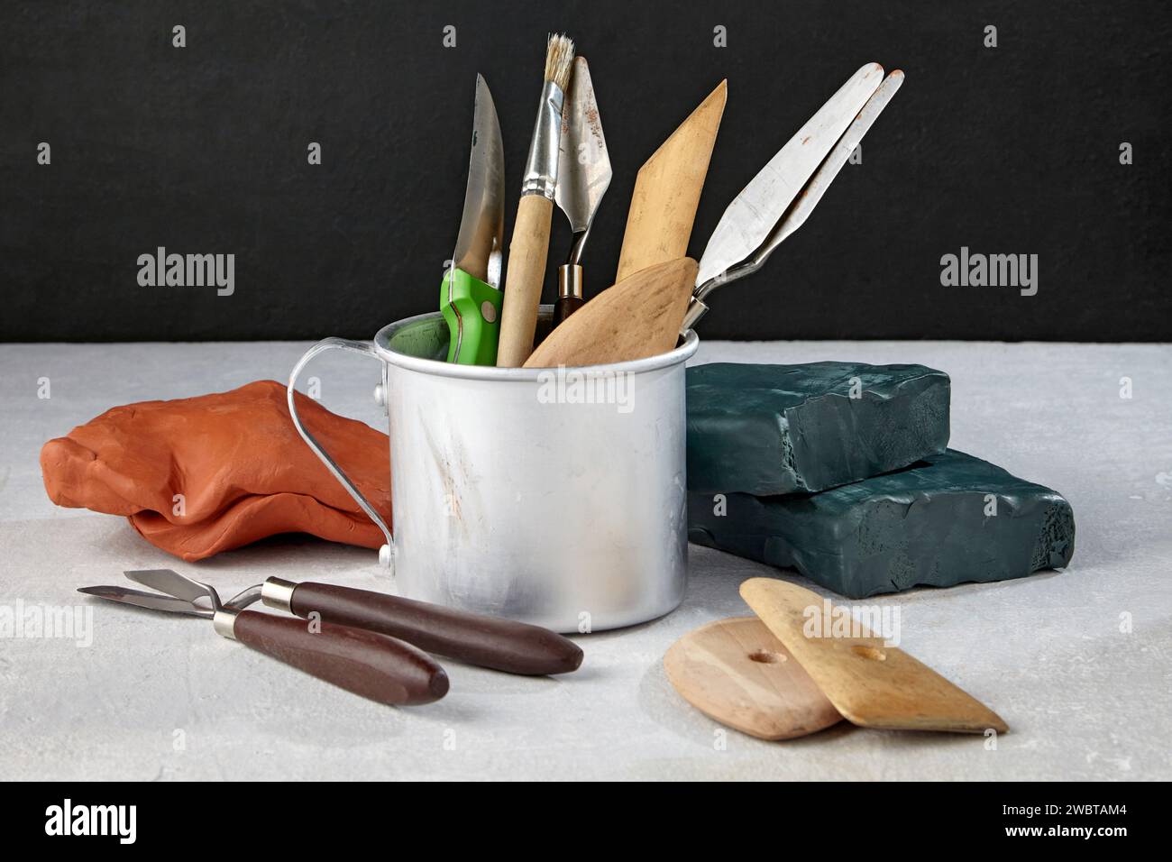 Verschiedene Bildhauerwerkzeuge für Modellierung und Stücke von Ton und Plastilin auf einem hellen Tisch mit dunklem Hintergrund Stockfoto