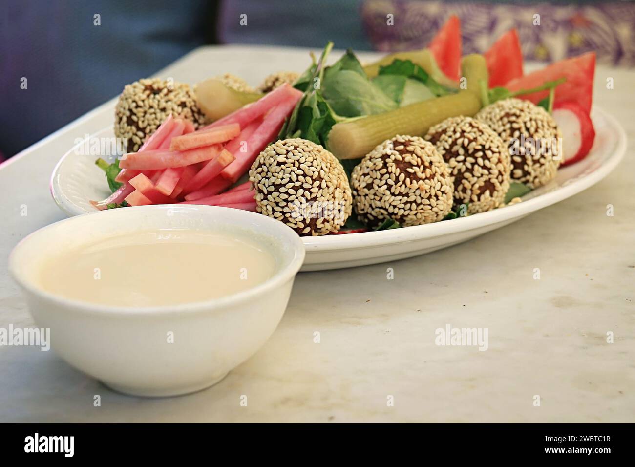 Falafelbällchen mit Sesam auf einer Platte zusammen mit dem traditionellen begleitenden Gemüse und Tahini-Sauce. Stockfoto