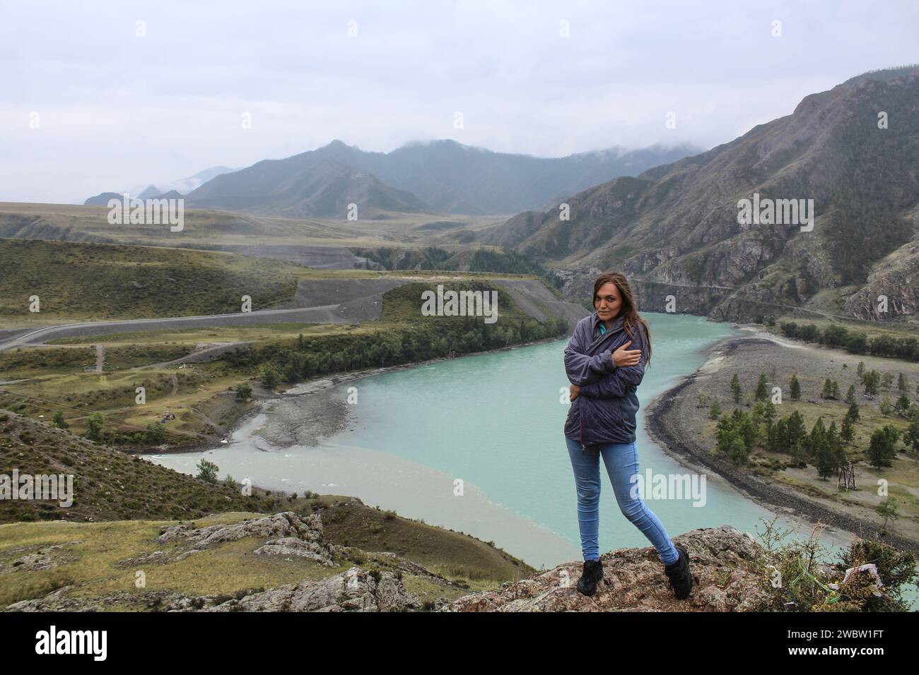 Concept Woman reist auf einer Alleinreise, stehend auf einem Hügel nahe dem Zusammenfluss von zwei Flüssen in verschiedenen Farben Chuya und Katun zu einem. Berglandschaft, Altai Republik, Russland. Stockfoto