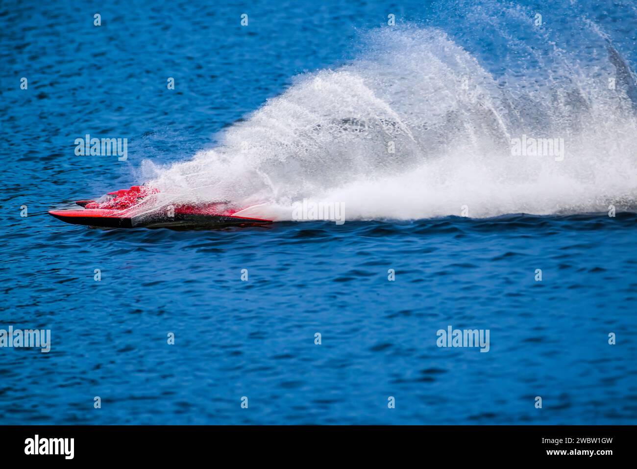 Das RC-Rennboot springt direkt über das Wasser und hinterlässt riesige Sprühnebel und Kräuselungen. Stockfoto