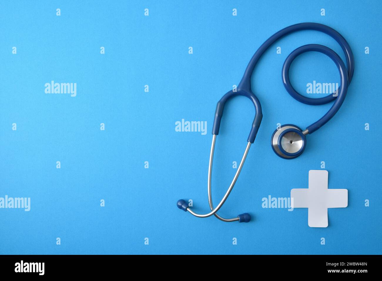 Allgemeinmedizinisches Konzept mit Stethoskop und Weißpapier kreuzförmig auf blauem Hintergrund. Draufsicht Stockfoto