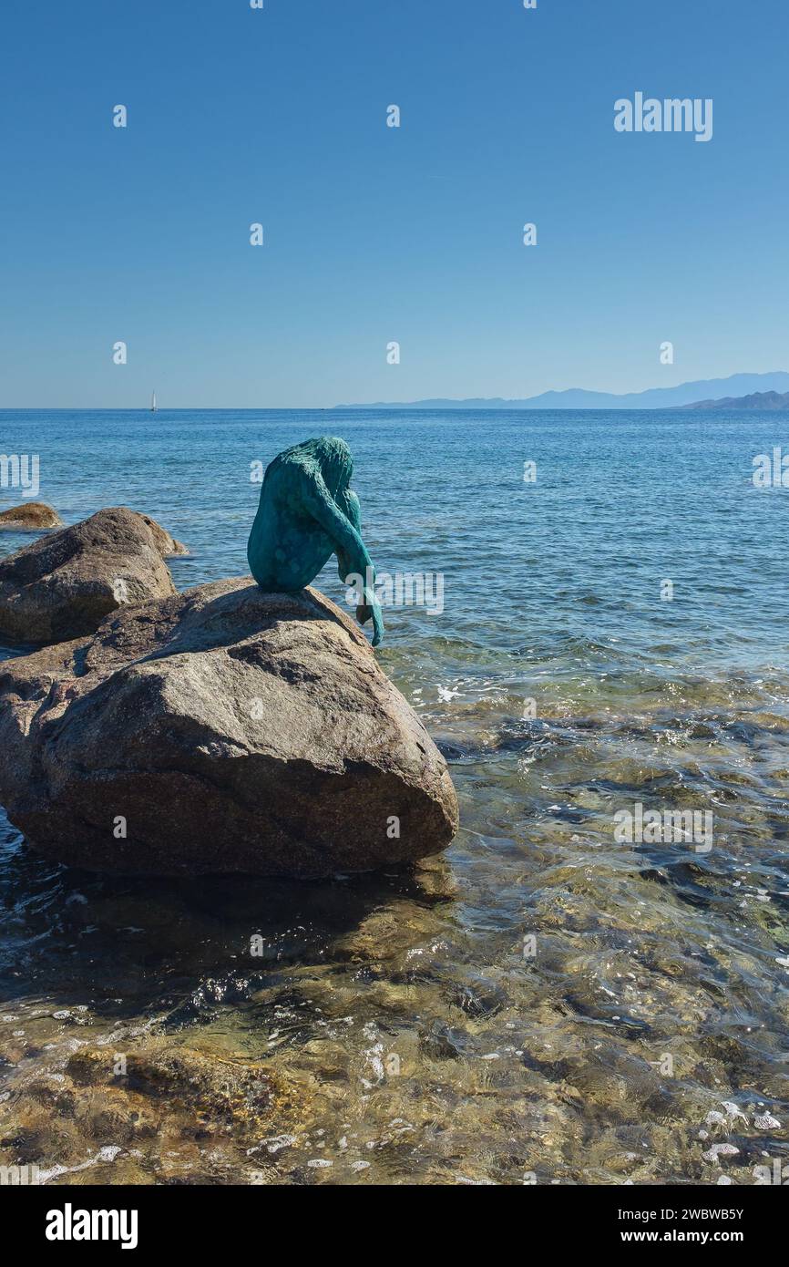 Ile Rousse, Korsika, 2017. Eine Sirenella di l'Isula Rossa, eine bronzene Meerjungfrau, die auf einem Felsen sitzt, der von den Wellen geschlagen wird. Statue von Gabriel Diana (vertikal) Stockfoto