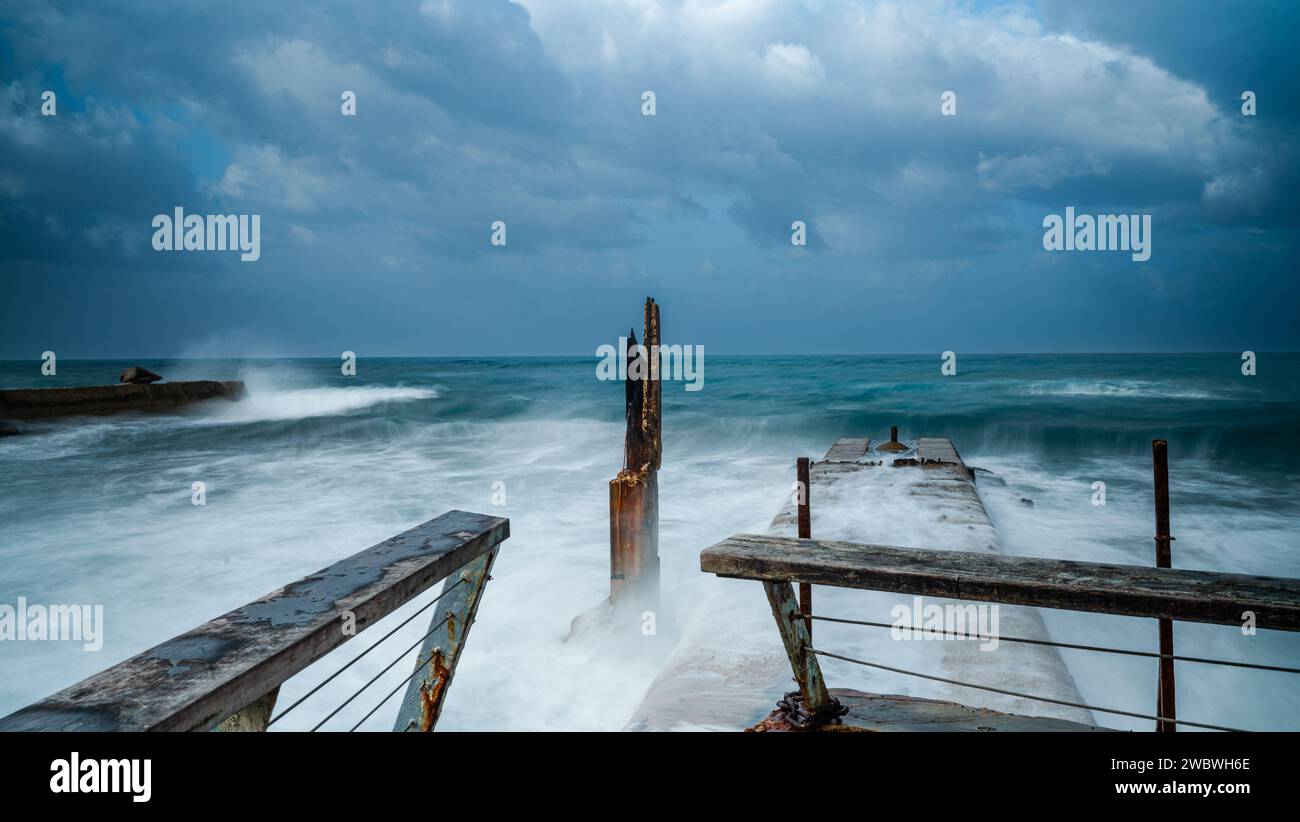 Ein hölzerner Pier, umgeben von der Kraft hoher Wellen und stürzenden Wellen, schafft eine dramatische und fesselnde Szene Stockfoto