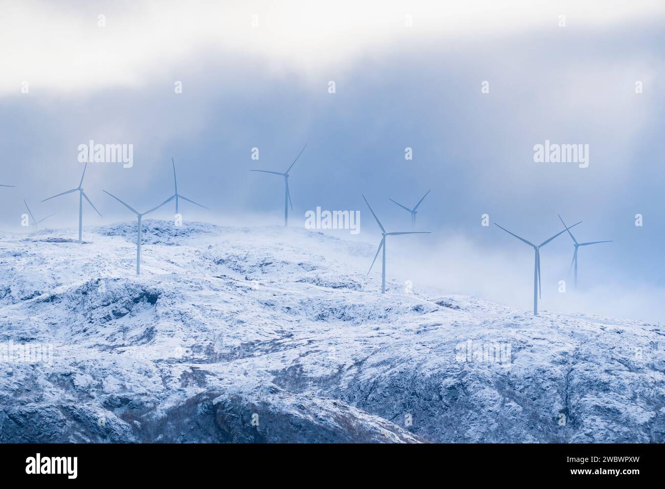 Windmühlen an der Atlantikküste bei jedem Wetter. Blick auf die frisch verschneiten Berge von der Insel Kvaløya, Norwegen, mit vielen Windturbinen Stockfoto