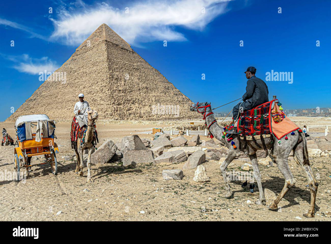 Gizeh Necropolis, Ägypten - 26. April 2022: Beduinenmänner in traditionellen Kleidern reiten auf Kamelen, die mit speziellen Stickereien verziert sind. Stockfoto