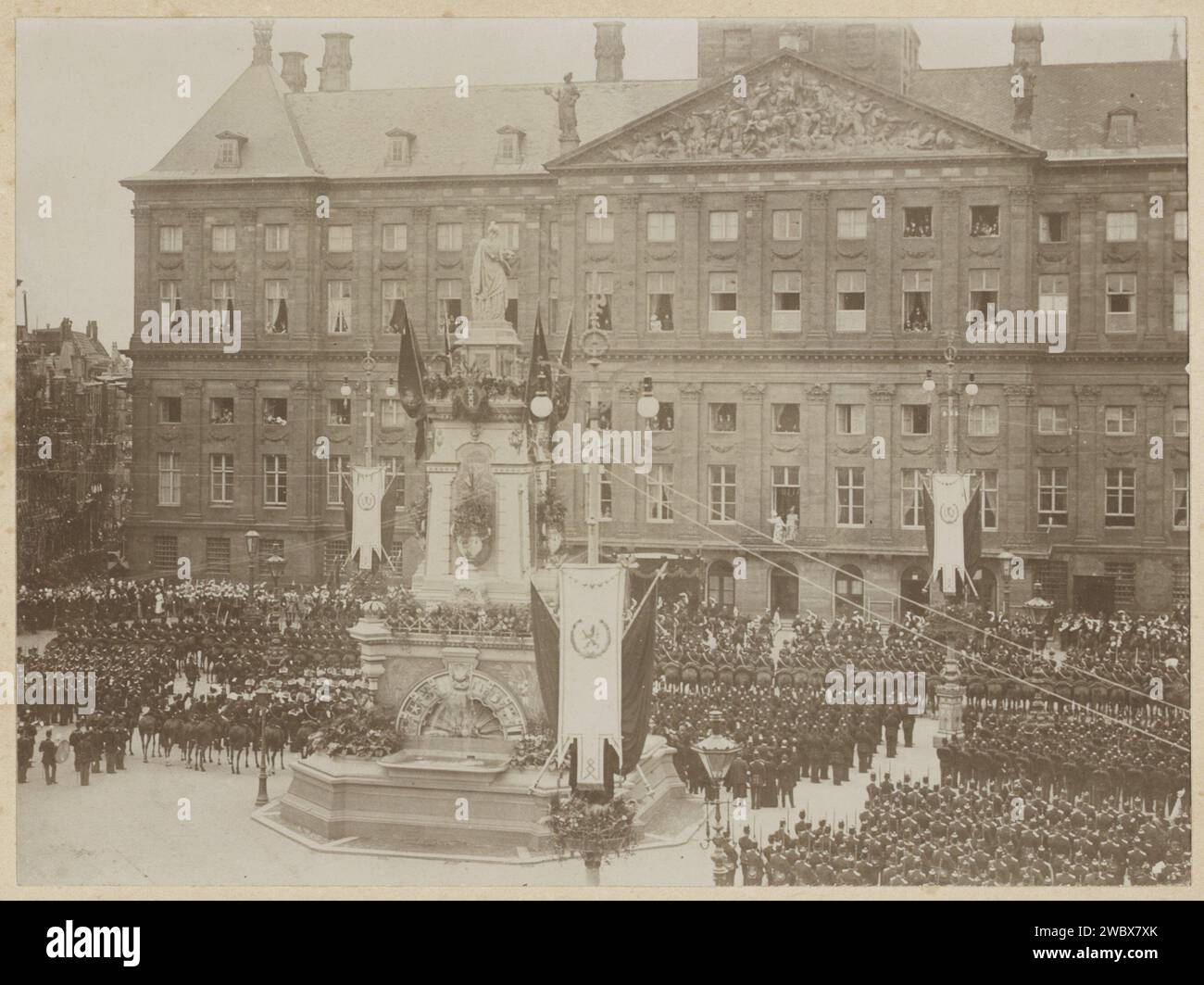 Militärgrüße an die eingeweihte Königin Wilhelmina und Königin Mutter Emma, die beide auf dem Balkon des Königspalastes auf dem Damplatz stehen, 1898 Foto Königin Wilhelmina und ihre Mutter Emma sind an der Schlossbar. Soldaten, die in der Linie aufgestellt wurden, bevölkerten den Platz. Im Vordergrund ein geschmückter Laternenpfahl und das Denkmal zur Erinnerung an den Volksgeist von 1830–1831, ausgezeichnet durch das Bild de Eendracht, bekannt als Naatje auf dem Damplatz. Teil des Fotoalbums mit 11 Aufnahmen der Einweihung der Königin Wilhelmina und der Einweihungsparteien. Dam-Karton. Papier. Fotografische Unterstützung historischer p Stockfoto