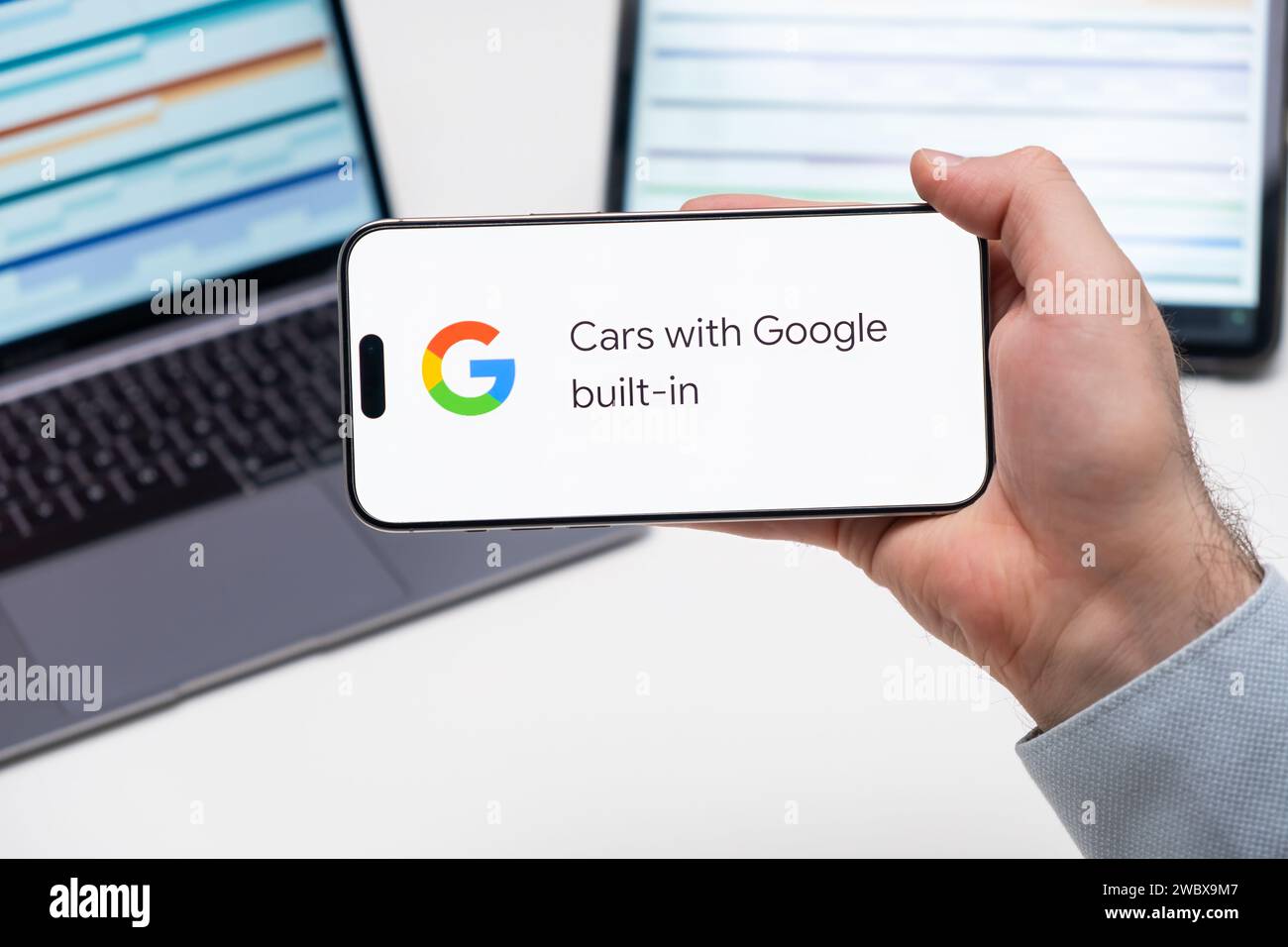 Autos mit Google Built in Application Logo auf dem Bildschirm des Smartphones in der Hand, Laptop und Tablet sind auf dem Tisch im Hintergrund, Dezember 2023, Prag, Tschechische Republik. Stockfoto