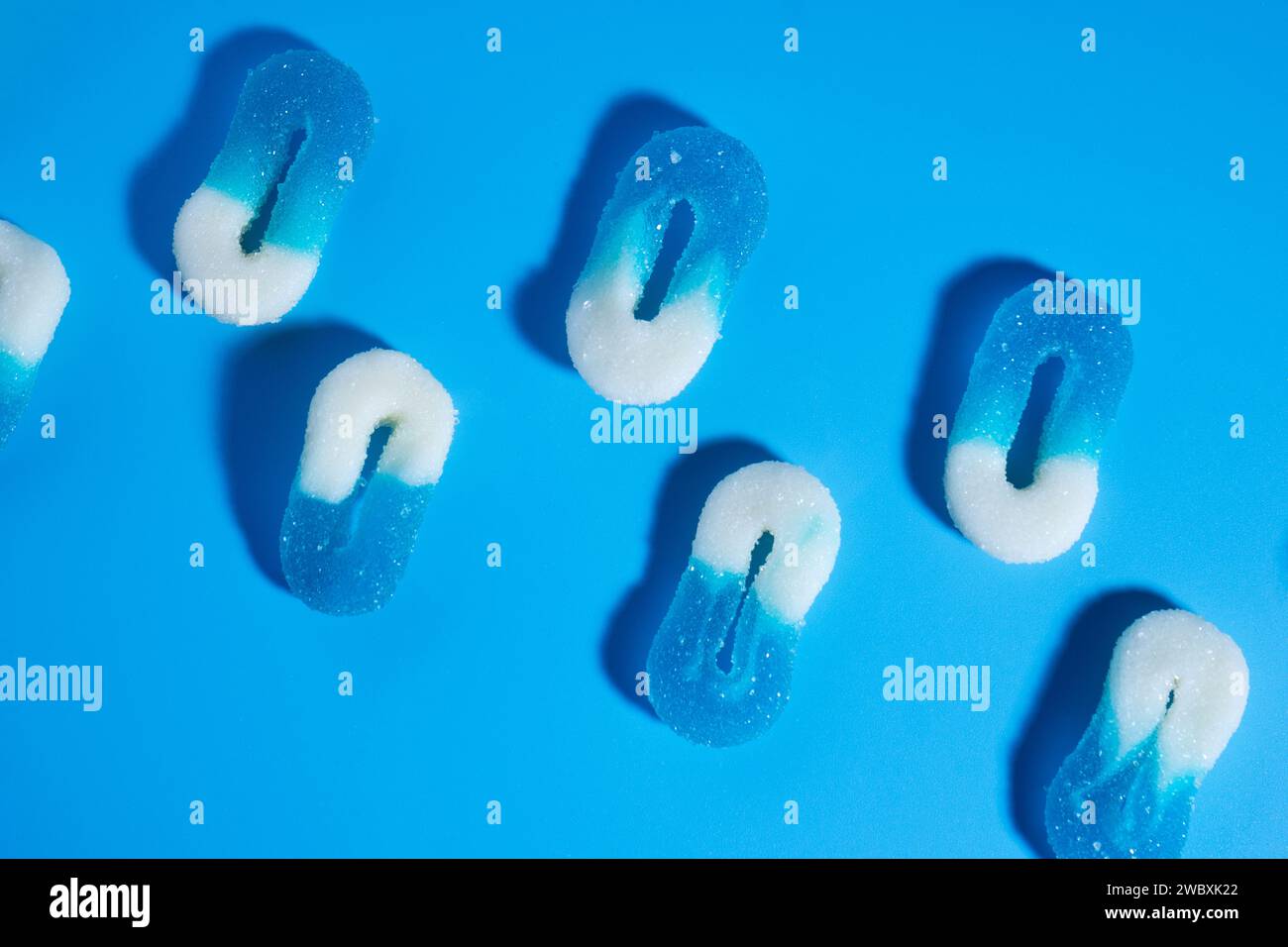 Array aus zwei Linien von 0-förmigen weißen und blauen gummiartigen Bonbons auf blauem Hintergrund, die in einer Diagonale in einem horizontalen Bild mit rauem Licht liegen. Positiv Stockfoto
