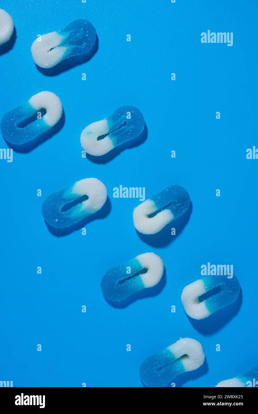 Array aus zwei Linien von 0-förmigen weißen und blauen gummiartigen Bonbons auf blauem Hintergrund, die in einer Diagonale in einem vertikalen Bild mit rauem Licht liegen. Upside VI Stockfoto
