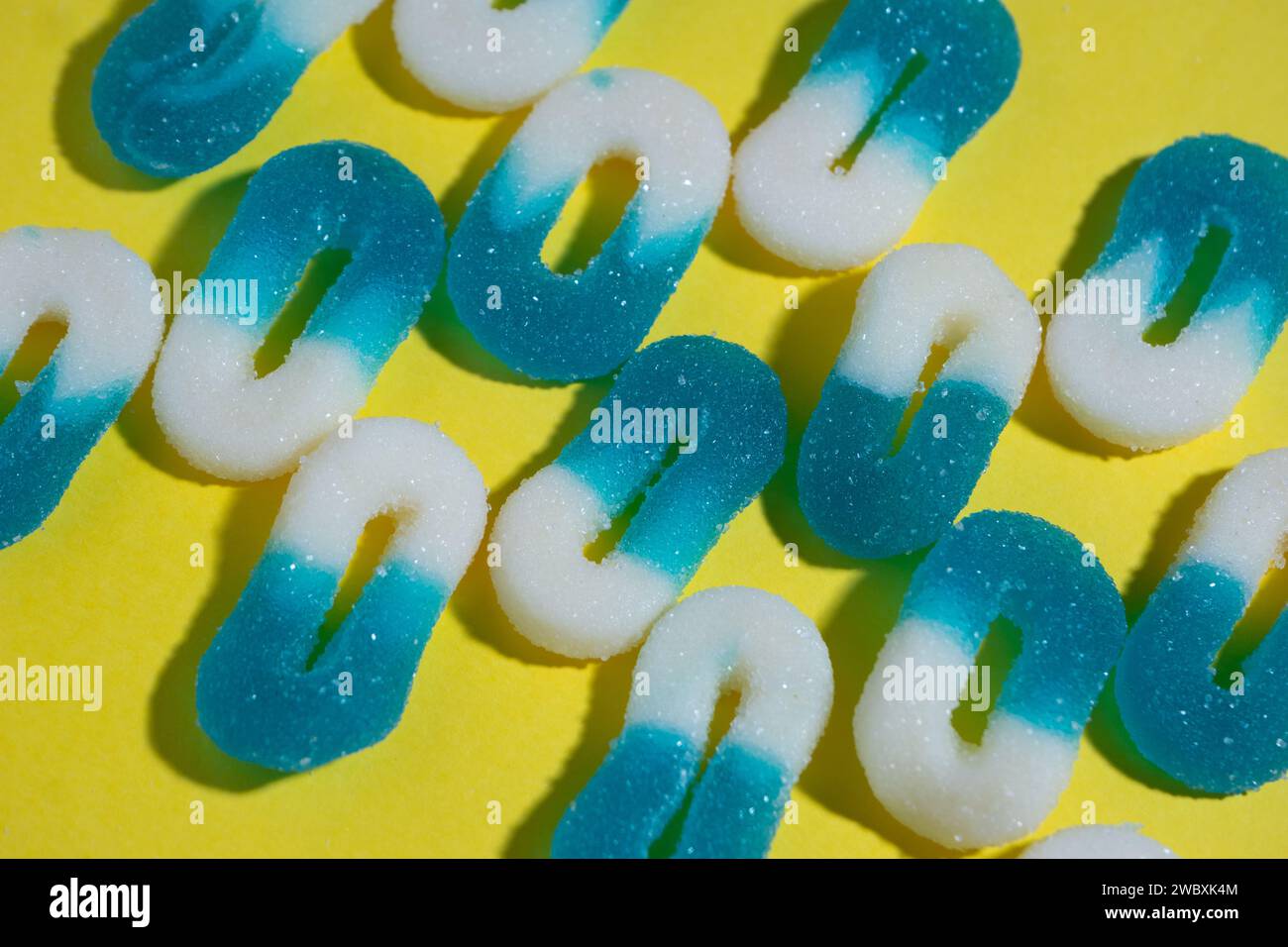 Anordnung mehrerer Linien mit 0-förmigen weißen und blauen gummiartigen Bonbons auf gelbem Hintergrund, horizontales Bild mit rauem Licht. Geneigte Ansicht. Stockfoto