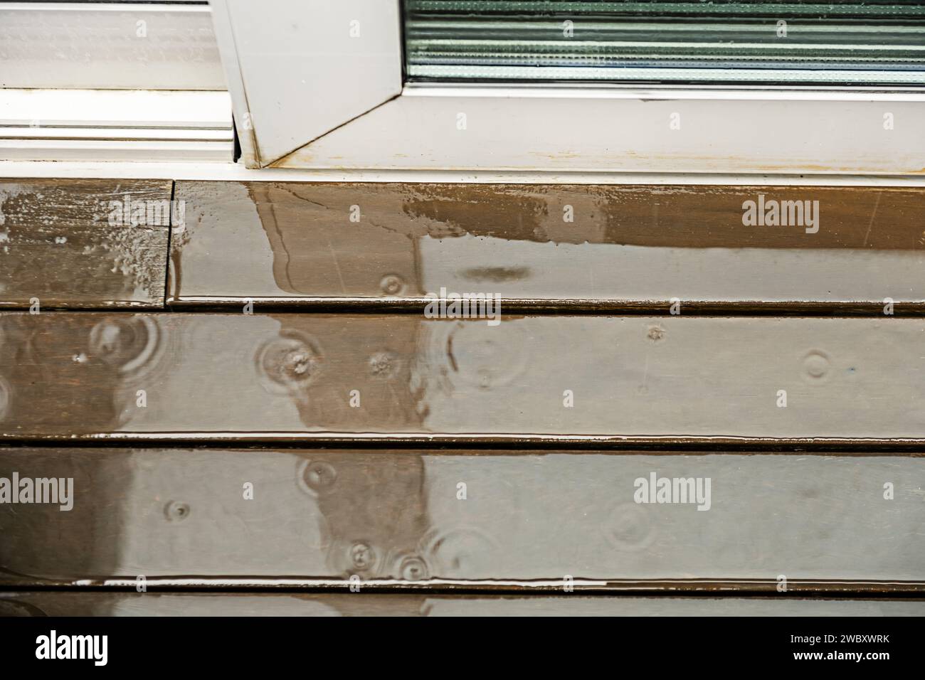 Holzdiele auf einer Terrasse, die mit Regenwasser und den Wellen gefüllt ist, die von den Wassertropfen erzeugt werden. Stockfoto