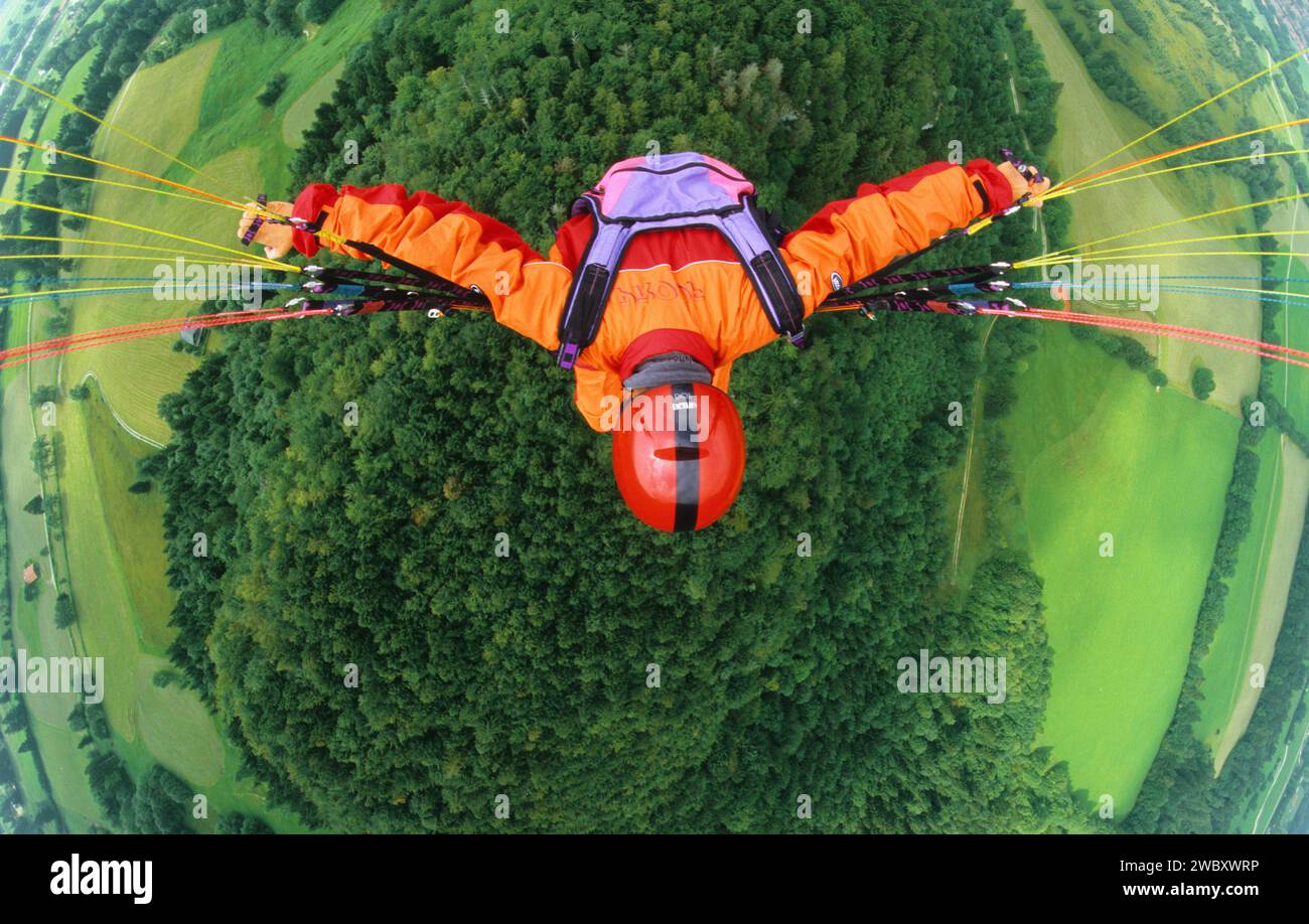 Gleitschirmflieger mit orangefarbener Kleidung und rotem Helm fliegt in 500 ft über Wald und Wiesen, Vogelperspektive, Brauneck, Lenggries, Bayern, Deutsch Stockfoto