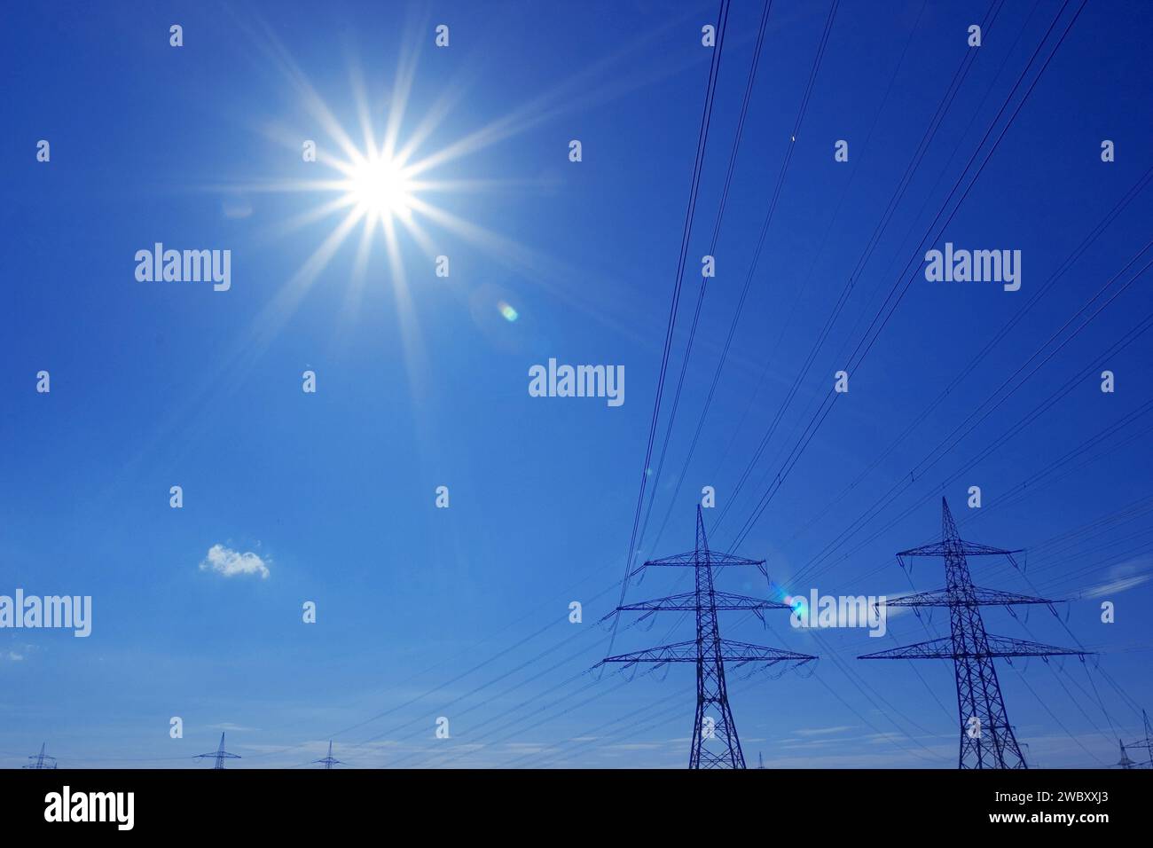 Hochspannungsleitung mit zwei Pylonen gegen blauen Himmel und Sonne Stockfoto