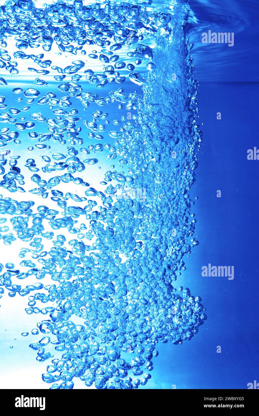 Nahaufnahme, Makro eines Wasserstrahls, der durch die Wasseroberfläche bricht und viele Luftblasen in einem Aquarium verursacht, blauer Hintergrund Stockfoto