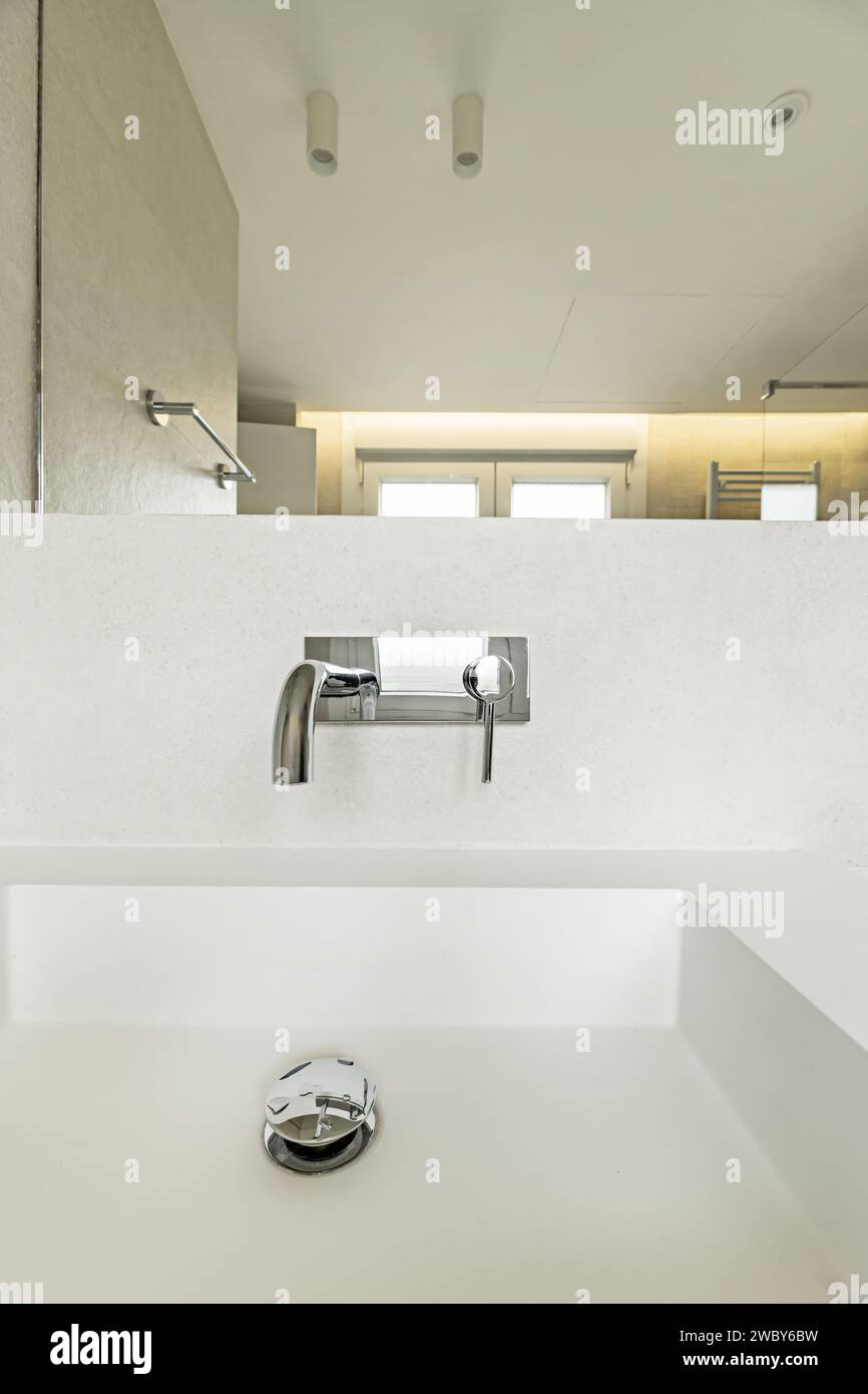 Ein modernes einteiliges Waschbecken mit Steinimitat und modernen Design-Armaturen, LED-Lampen an der Decke, Handtuchheizkörper und rahmenloser Spiegel an der Wand Stockfoto