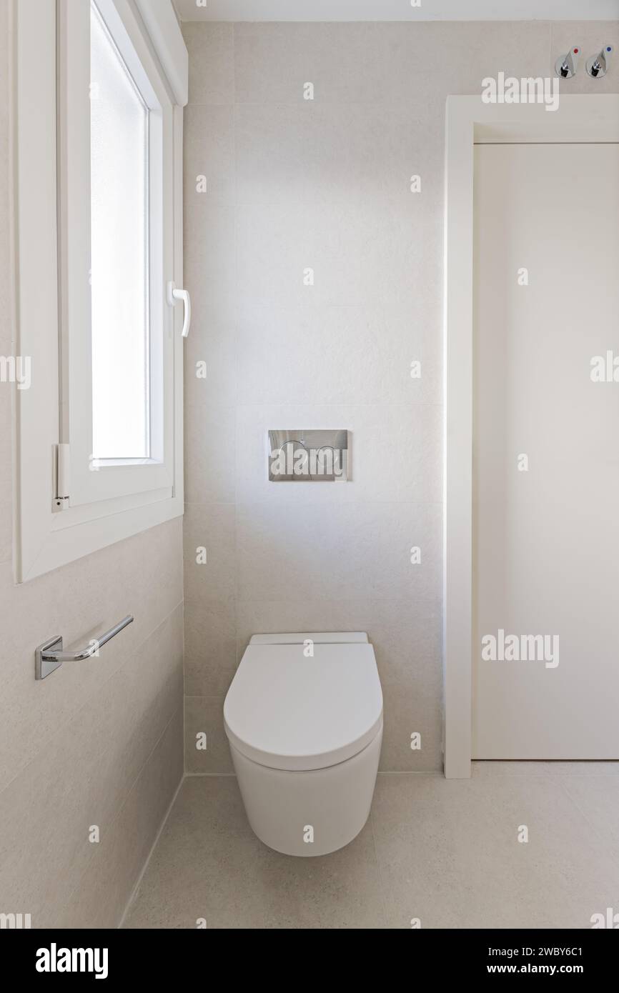 Neu gebautes kleines Badezimmer mit schwimmender Toilette neben einer weißen Holztür und Aluminiumfenster Stockfoto