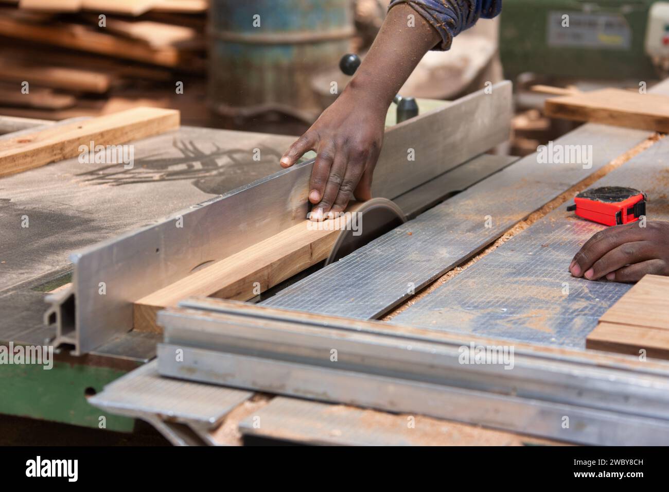 afrikanischer Mann, der mit einer Sägeblatt-Holzbearbeitungsmaschine in der Werkstatt arbeitet und Holz schneidet Stockfoto