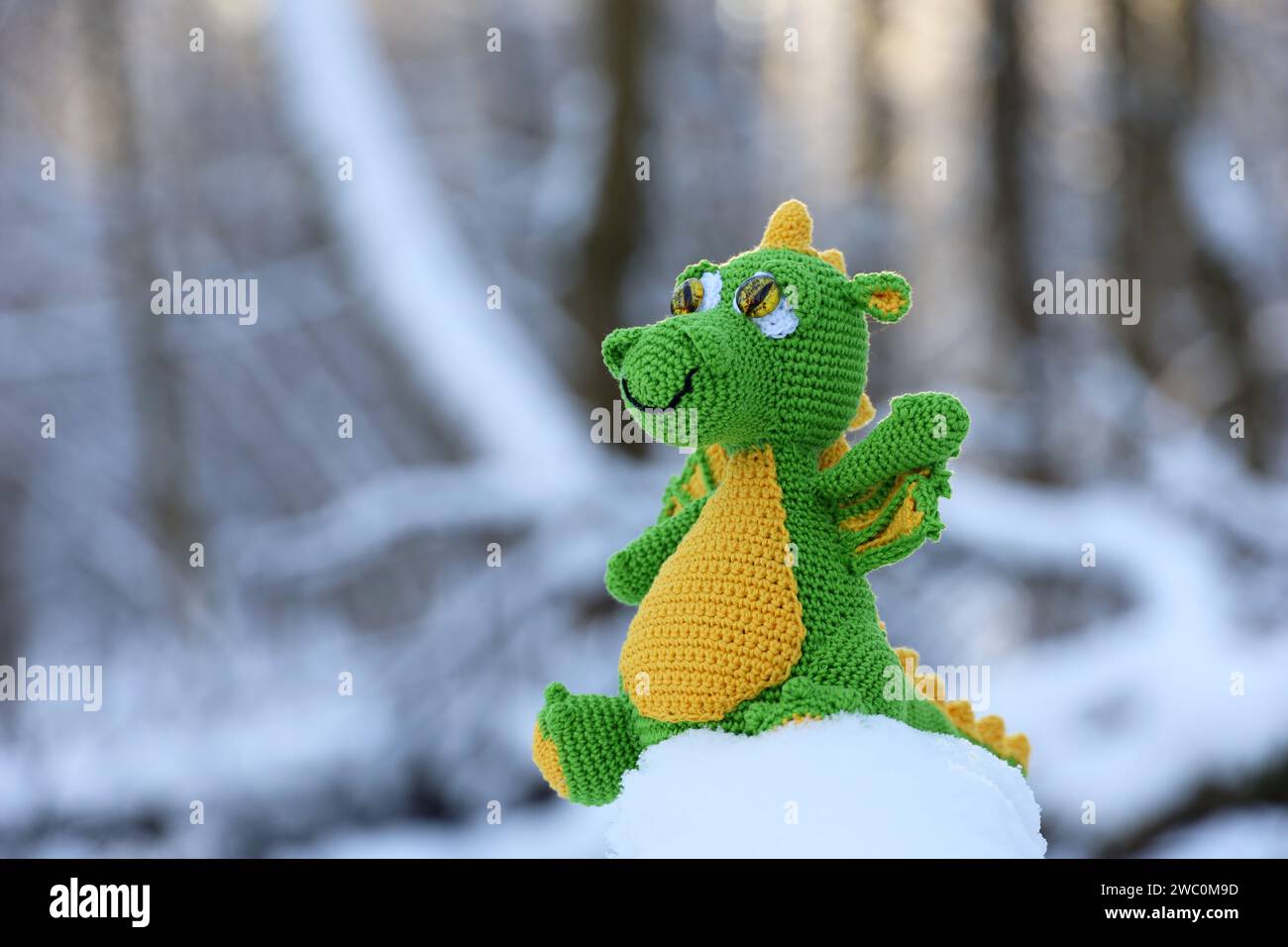 Gestrickter Drache in einem Schnee auf Winterwald Hintergrund, Grußkarte. Symbol des chinesischen Neujahrs 2024 Stockfoto