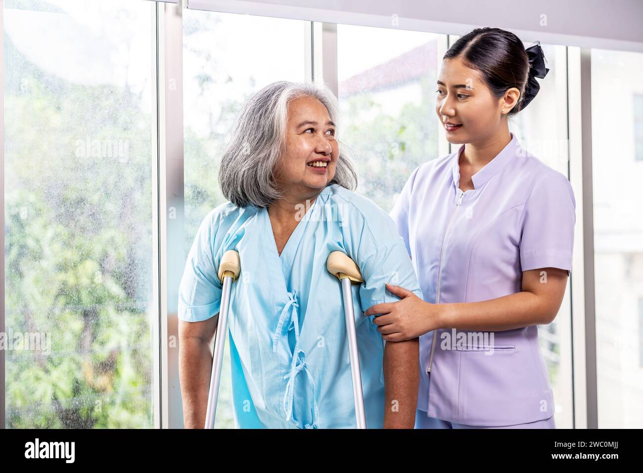 Eine aufmerksame Krankenschwester unterhält sich mit einer älteren Frau, indem sie Krücken zur Unterstützung verwendet Stockfoto