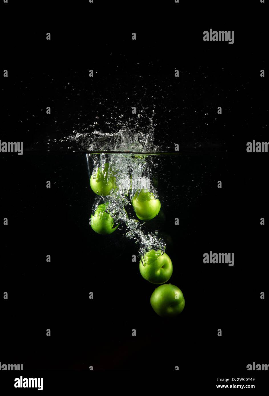 Grüne Pflaume fiel ins Wasser mit Blasen isoliert auf schwarzem Hintergrund. Stockfoto