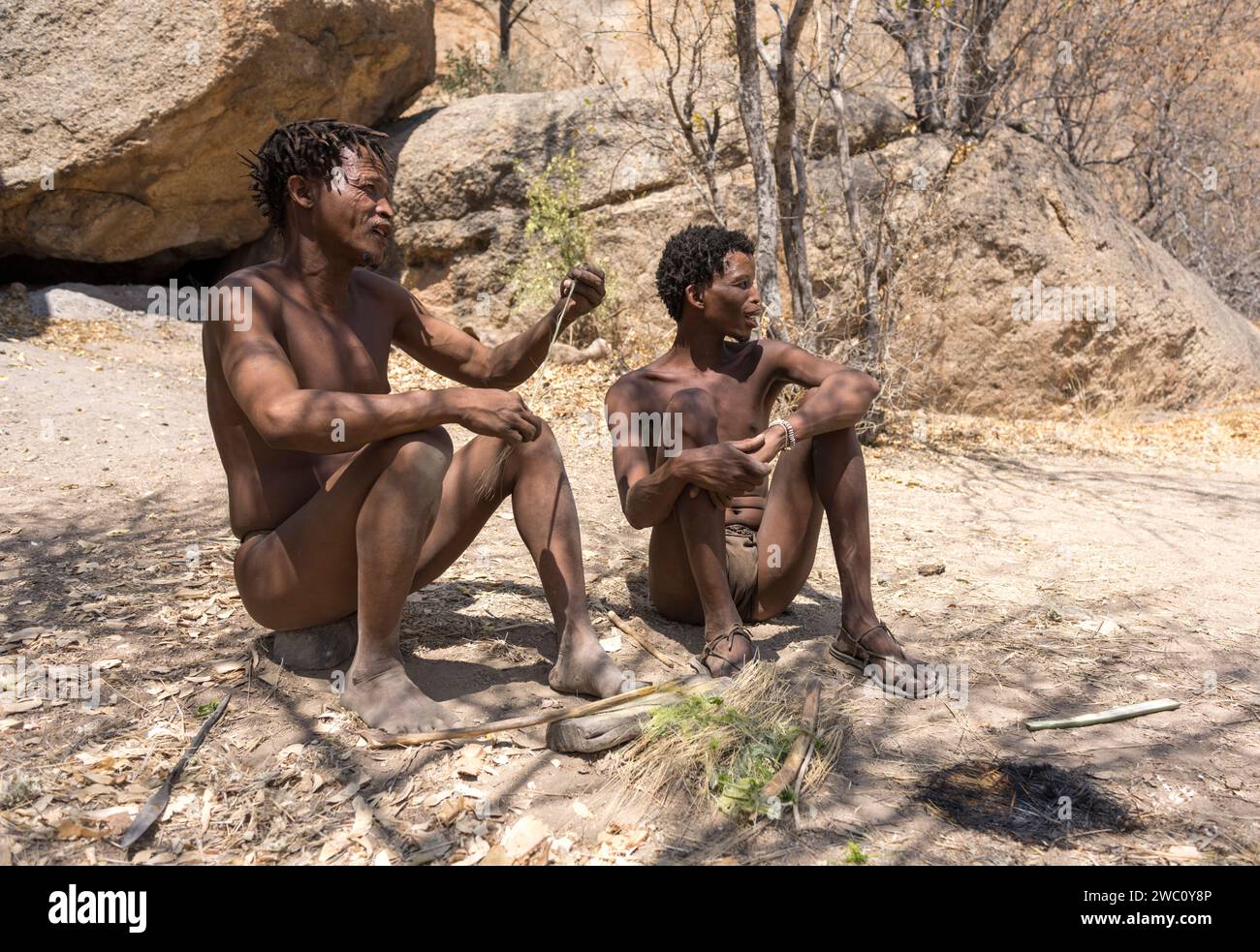 Zwei San Buschmänner sitzen zusammen auf dem Boden in einem traditionellen Camp in Namibia Stockfoto