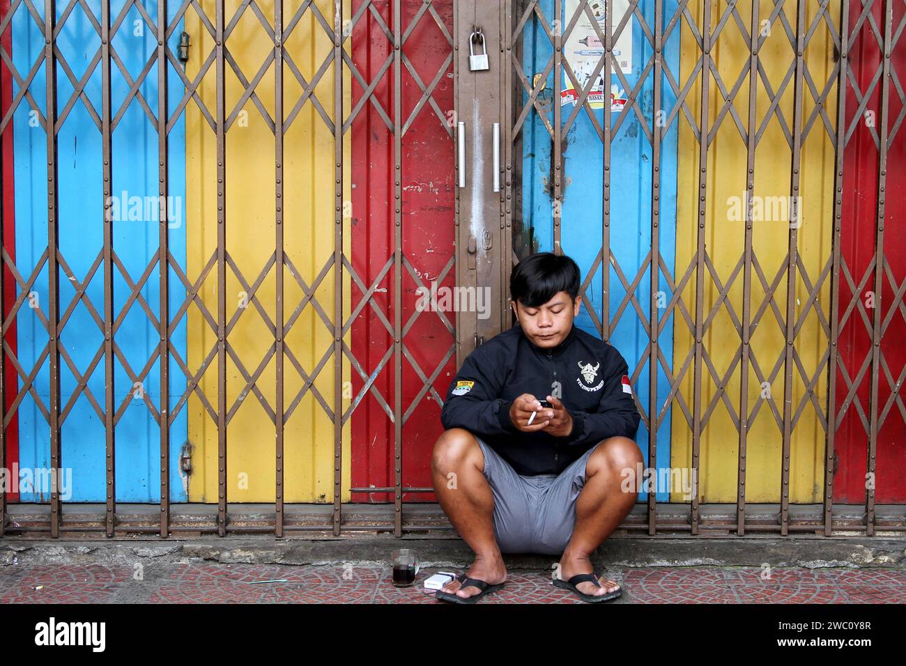 Ein Mann hockte sich auf dem Boden vor einem bunten Laden und rauchte eine Zigarette in Indonesien. Stockfoto