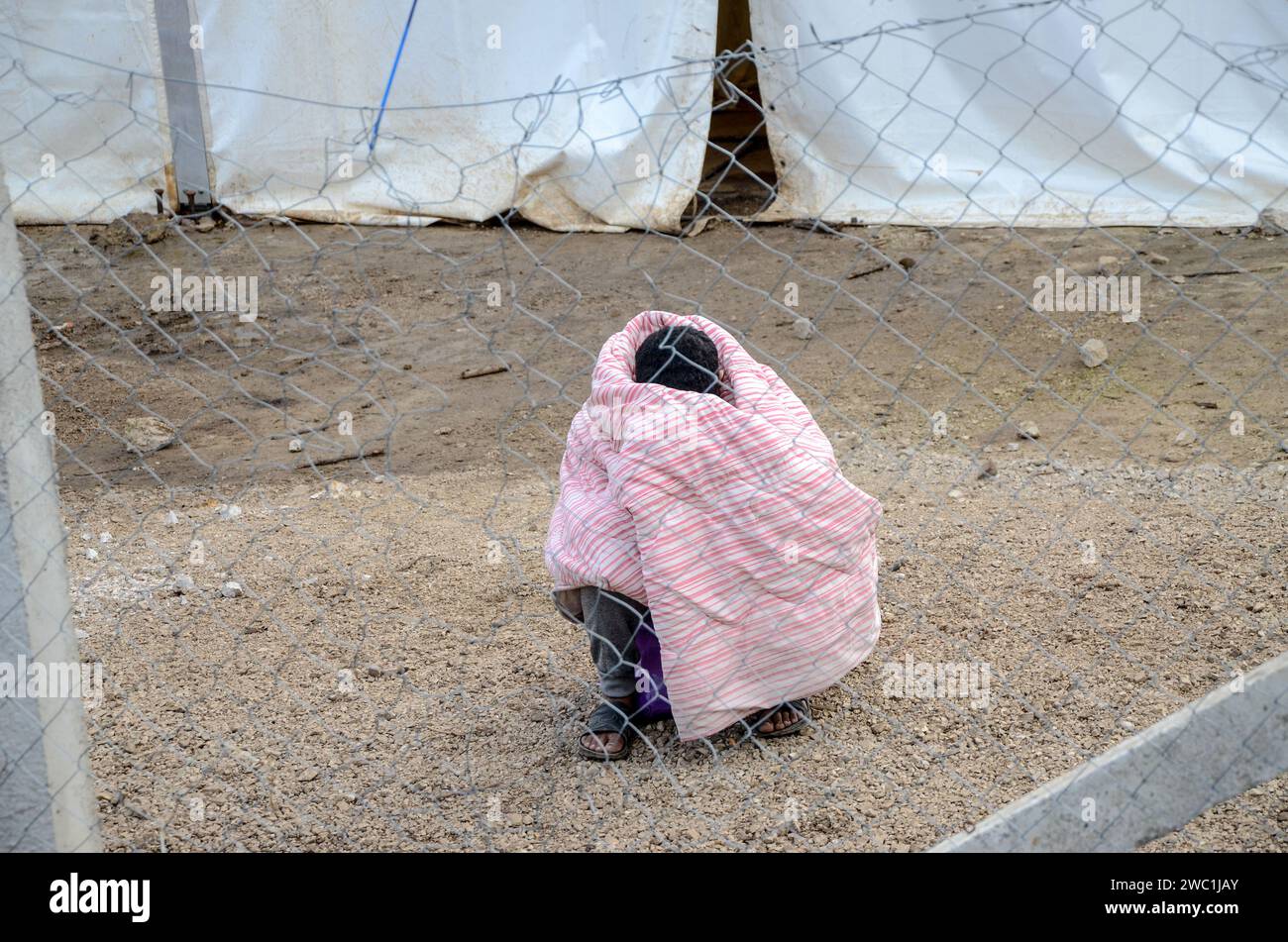 Der Migrant friert im Lager ein, eingezäunt mit Draht. Mann in eine Decke gewickelt. Flüchtlingsfrieren im Winter im Lager in Bihac, Bosnien und Herzegowina. Stockfoto