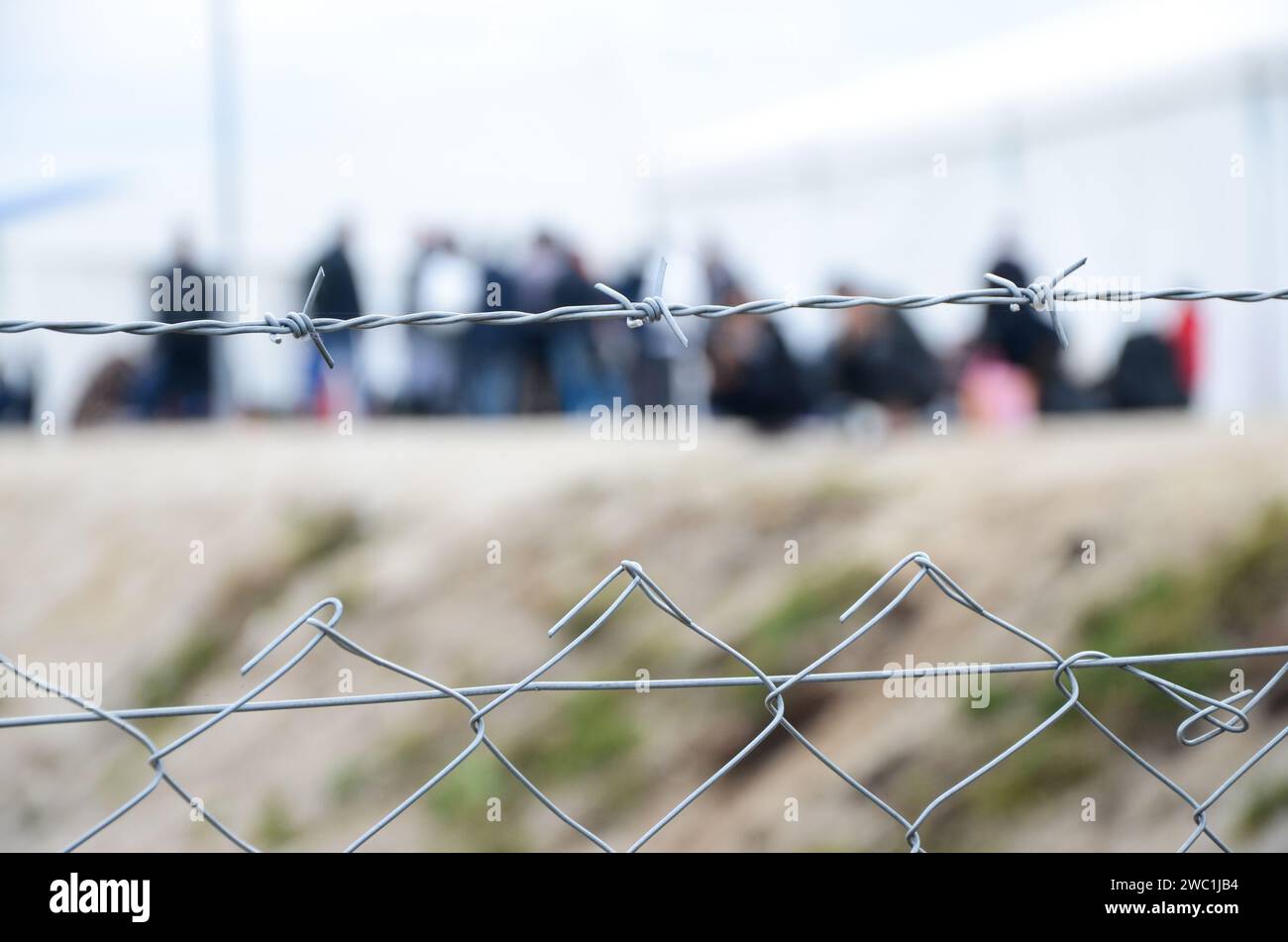 Stacheldraht im Flüchtlingslager. Migranten hinter Maschendrahtzaun im Lager. Eine Gruppe von Leuten hinter dem Zaun. Das Konzept von Gefängnis, Freiheit, Barriere, Migration. Stockfoto