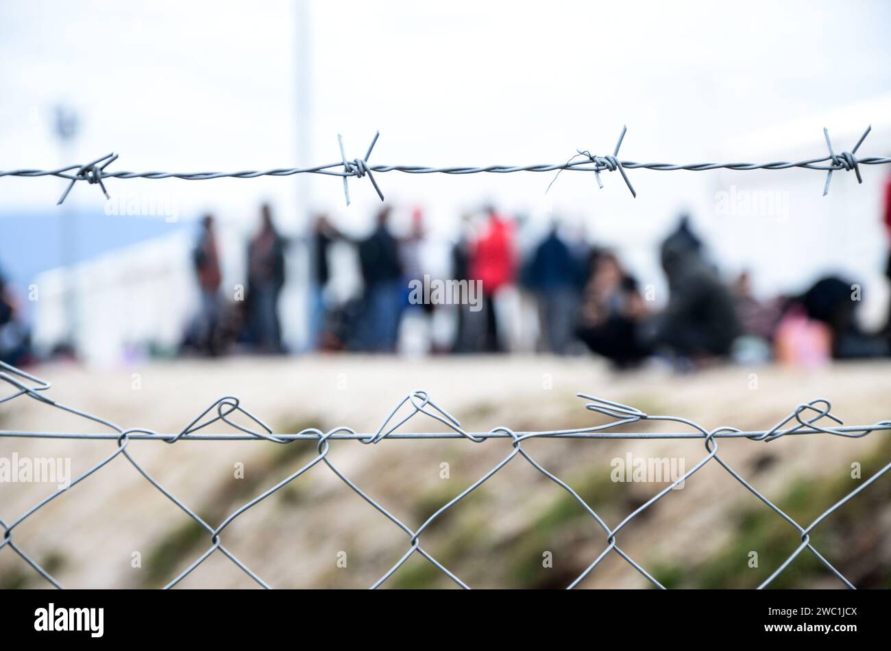 Stacheldraht im Flüchtlingslager. Migranten hinter Maschendrahtzaun im Lager. Eine Gruppe von Leuten hinter dem Zaun. Das Konzept von Gefängnis, Freiheit, Barriere, Migration. Stockfoto
