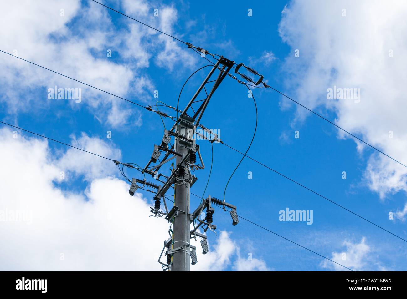 Mittelspannungs-Freileitung, Mast mit Isolatoren und Trennschaltern, weiße Wolken am blauen Himmel Stockfoto