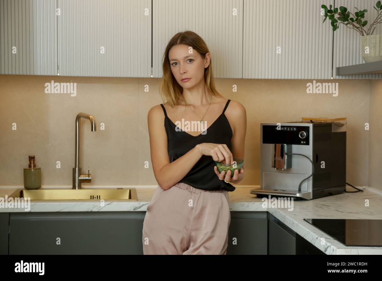Eine junge ernste Frau, die in der Küche einen kleinen Snack hat. Diätetisches Restriktionskonzept. Stockfoto