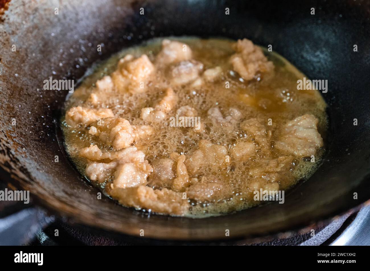 Knusprig gebratenes Hühnerfleisch mit kochendem Öl in einer traditionellen, gealterten Pfanne auf einem Gasherd braten Stockfoto