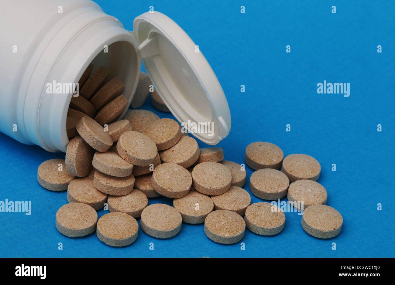 Medizin und Gesundheitskonzept. Gelb-braune Pillen Nahaufnahme. Aus einer weißen Plastikflasche verschüttete Pillen. Stockfoto