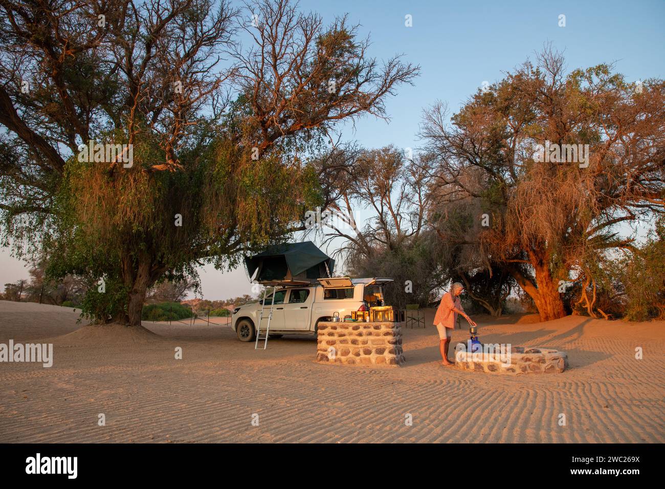 Ein Camper bereitet das Abendessen bei Sonnenuntergang in einem Camp im felsigen Damaraland am Rande der Namib-Wüste im Erongo-Bezirk im Nordwesten Namibs zu Stockfoto