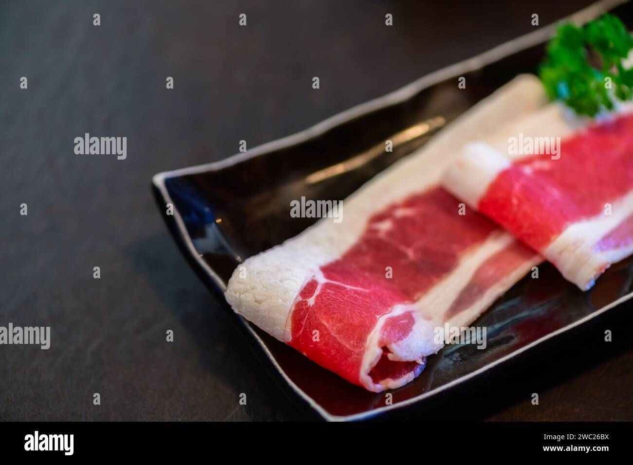 In Scheiben geschnittenes Wagyu marmoriertes Rindfleisch für Yakiniku auf Platte auf schwarzem Hintergrund, japanisches Premium-Fleischkonzept Stockfoto