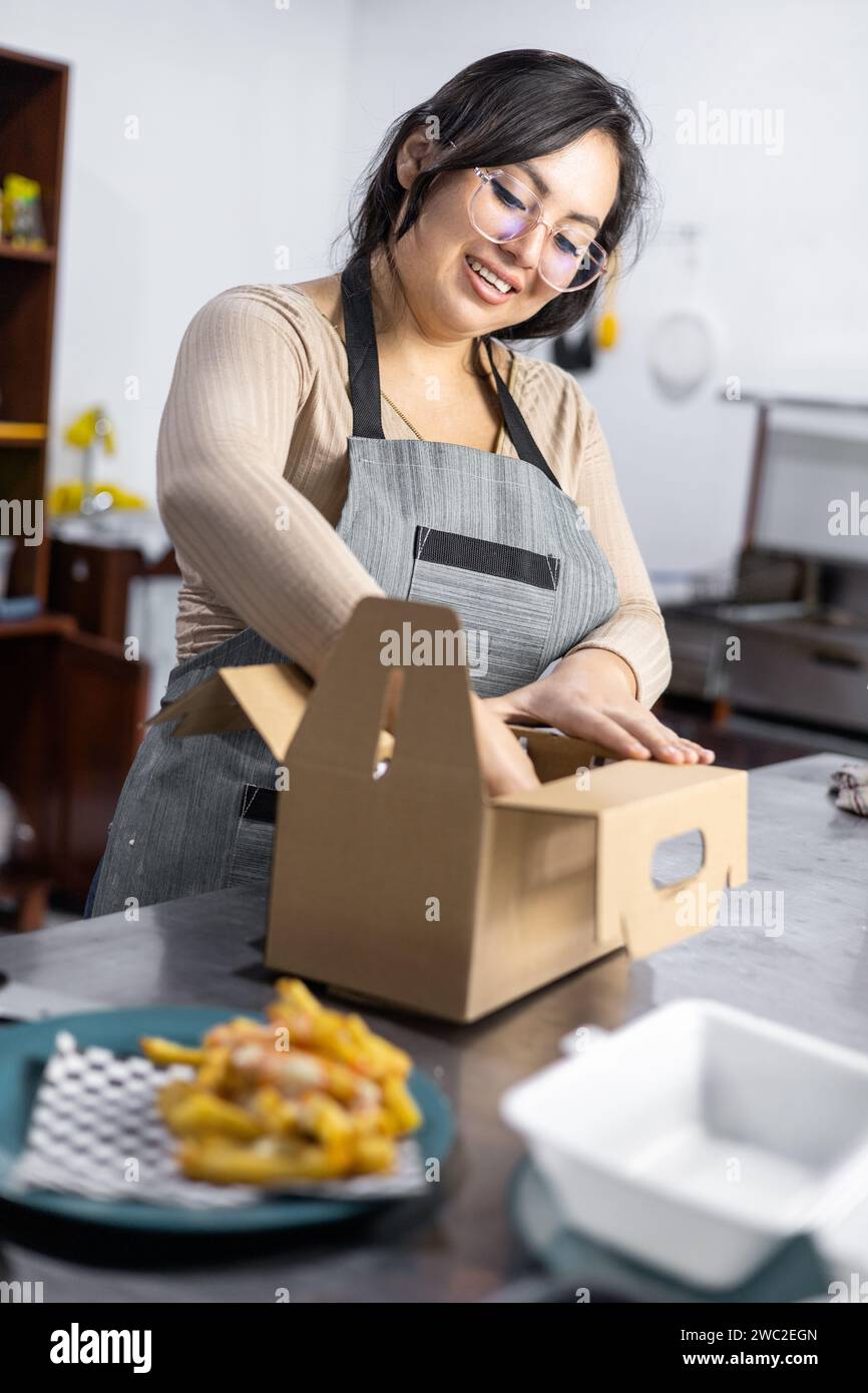 Frau, die einen Hamburger in einen Karton packt, Fast Food bereit zur Lieferung, Kundenservice und Restaurant Lifestyle, dunkle Küche Service Stockfoto