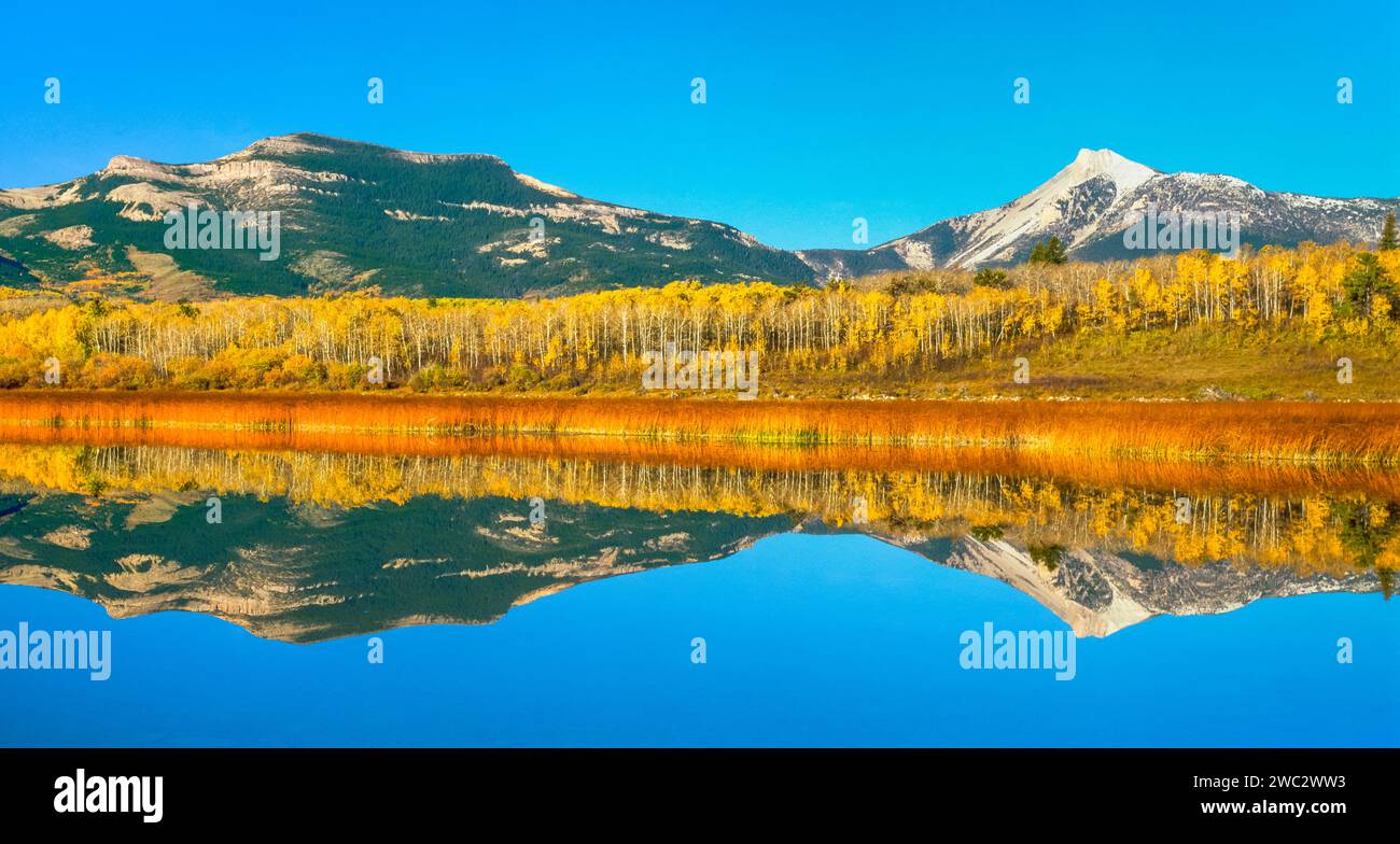 Panorama der Herbstfarben und der Federwoman Mountain entlang der felsigen Berghöhe, die sich in einem Teich in der Nähe von Heart butte, montana, widerspiegelt Stockfoto
