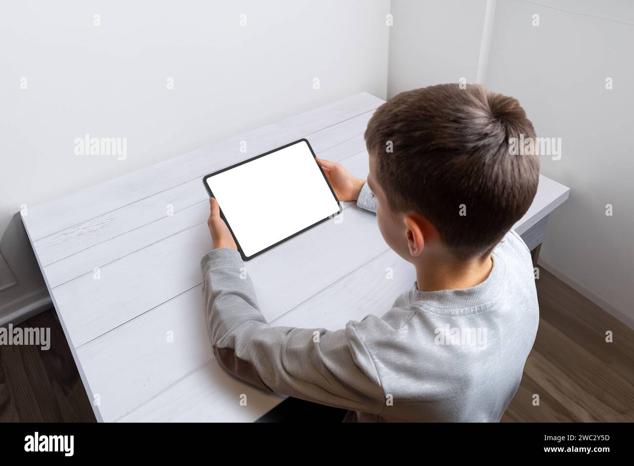 Boy Hold Tablet mit isoliertem Bildschirm für Spiel- oder App-Werbung auf einem aufgeräumten Schreibtisch. Perfekt für digitale Unterhaltung und Bildungsanwendungen Stockfoto