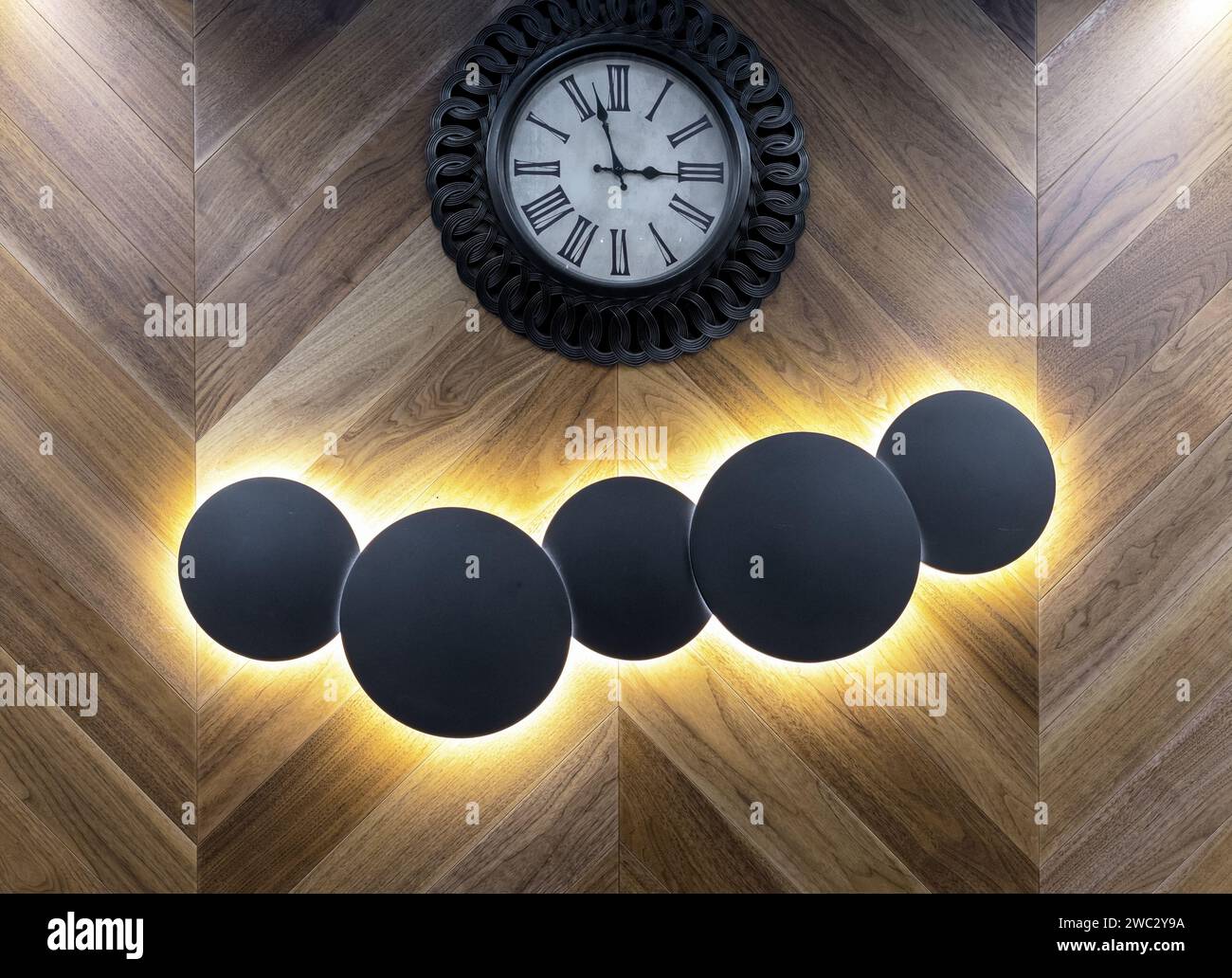 Runde beleuchtete Lampen?Unterdurchbrochene Beleuchtung an einer Holzwand mit einer Uhr. Stockfoto