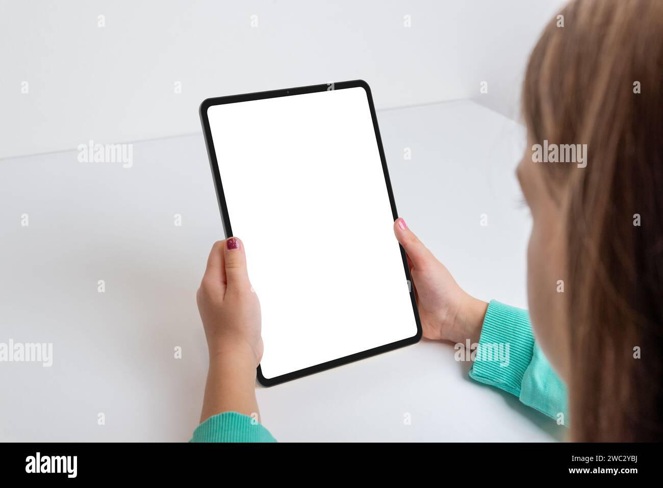Vertikales Tablet, das von einem Mädchen auf einem Schreibtisch gehalten wird. Perfekt für die Präsentation von Spielen oder Apps auf einem isolierten Bildschirm. Moderne Technik in den Händen eines Jungen Stockfoto
