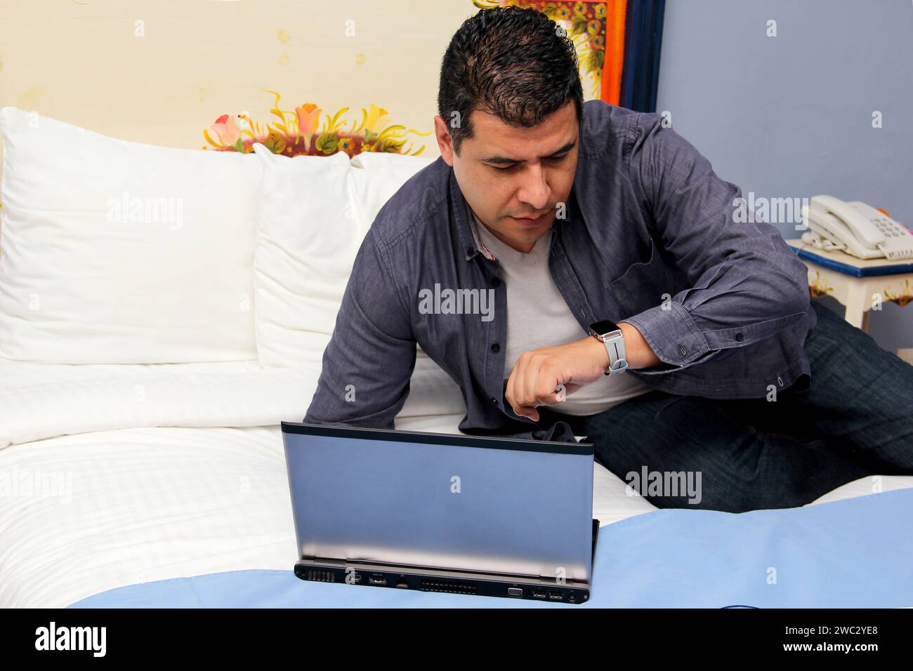 Der 40-jährige dunkelhäutige Latin-Mann arbeitet auf seinem Laptop auf dem Bett, arbeitet im Home Office und überarbeitet, was Stress verursacht Stockfoto
