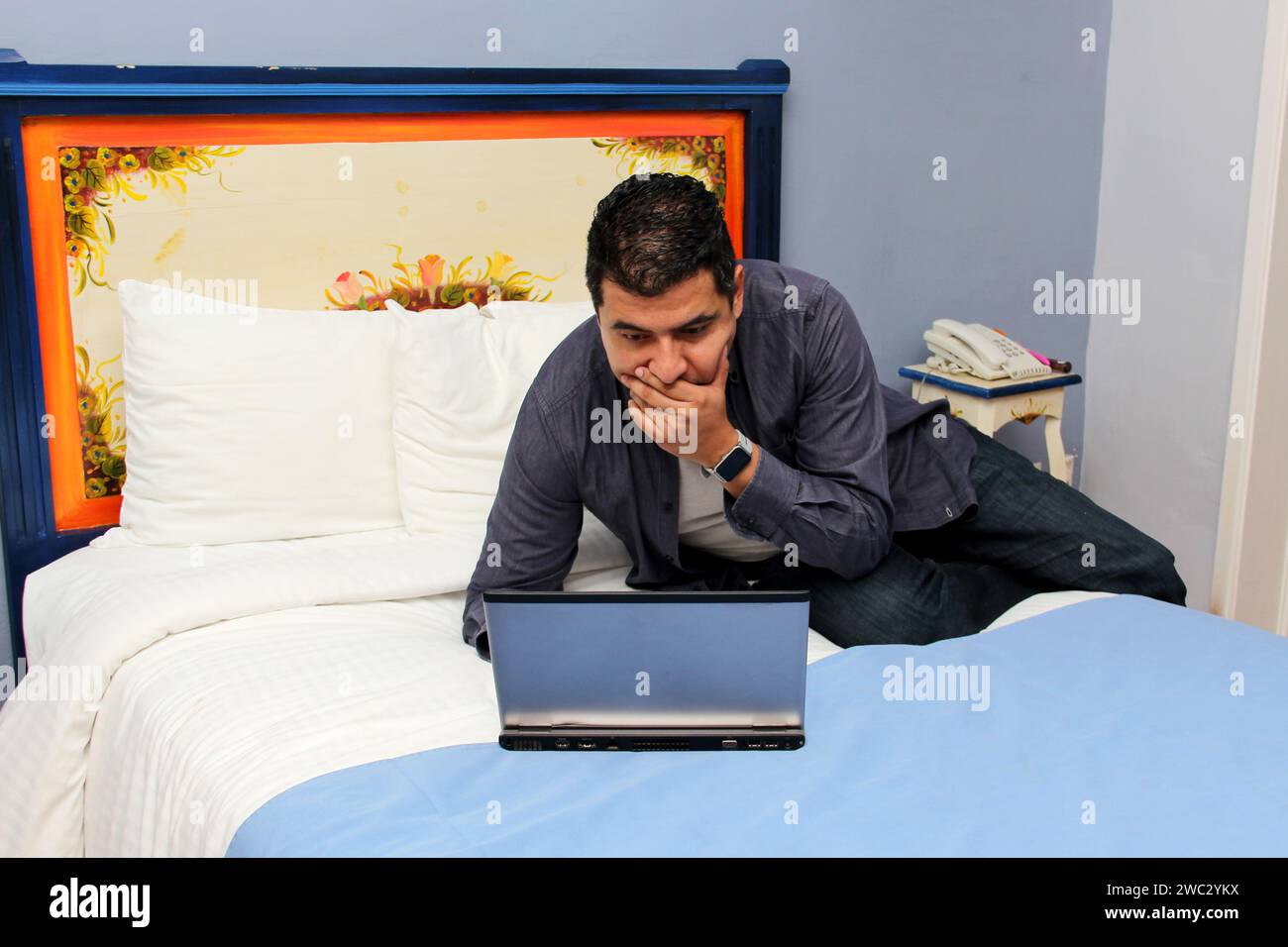 Der 40-jährige dunkelhäutige Latin-Mann arbeitet auf seinem Laptop auf dem Bett, arbeitet im Home Office und überarbeitet, was Stress verursacht Stockfoto