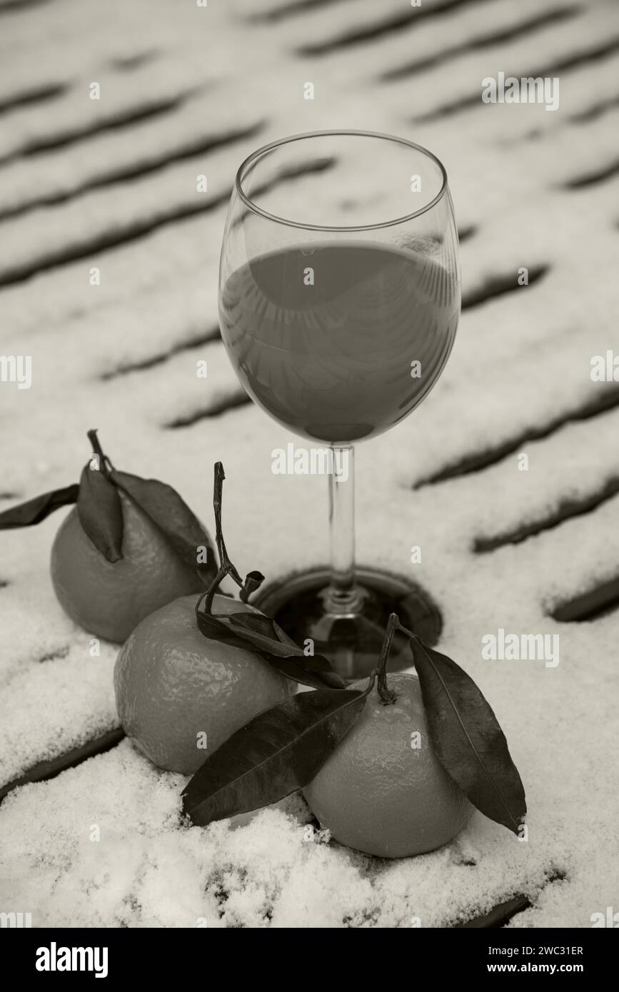 Glas frisch gepressten Bio-Mandarinensaft auf schneebedeckten Tisch im Garten und Mandarinenfrüchte. Gesunder Lebensstil Hintergrund. Sepia-Foto. Stockfoto