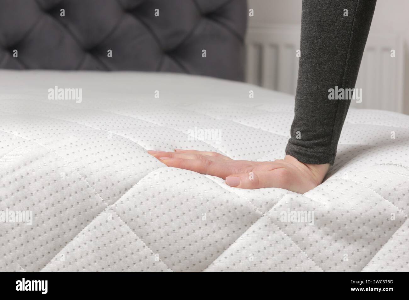 Frau drückt auf bequeme Matratze, überprüft und testet Qualität Stockfoto