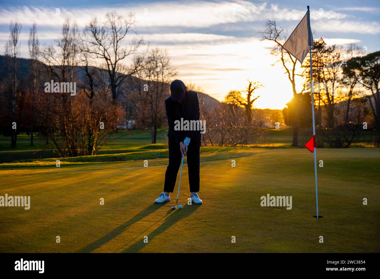 Weibliche Golferkonzentration auf dem Putting Green On Golfplatz bei Sonnenuntergang in der Schweiz Stockfoto